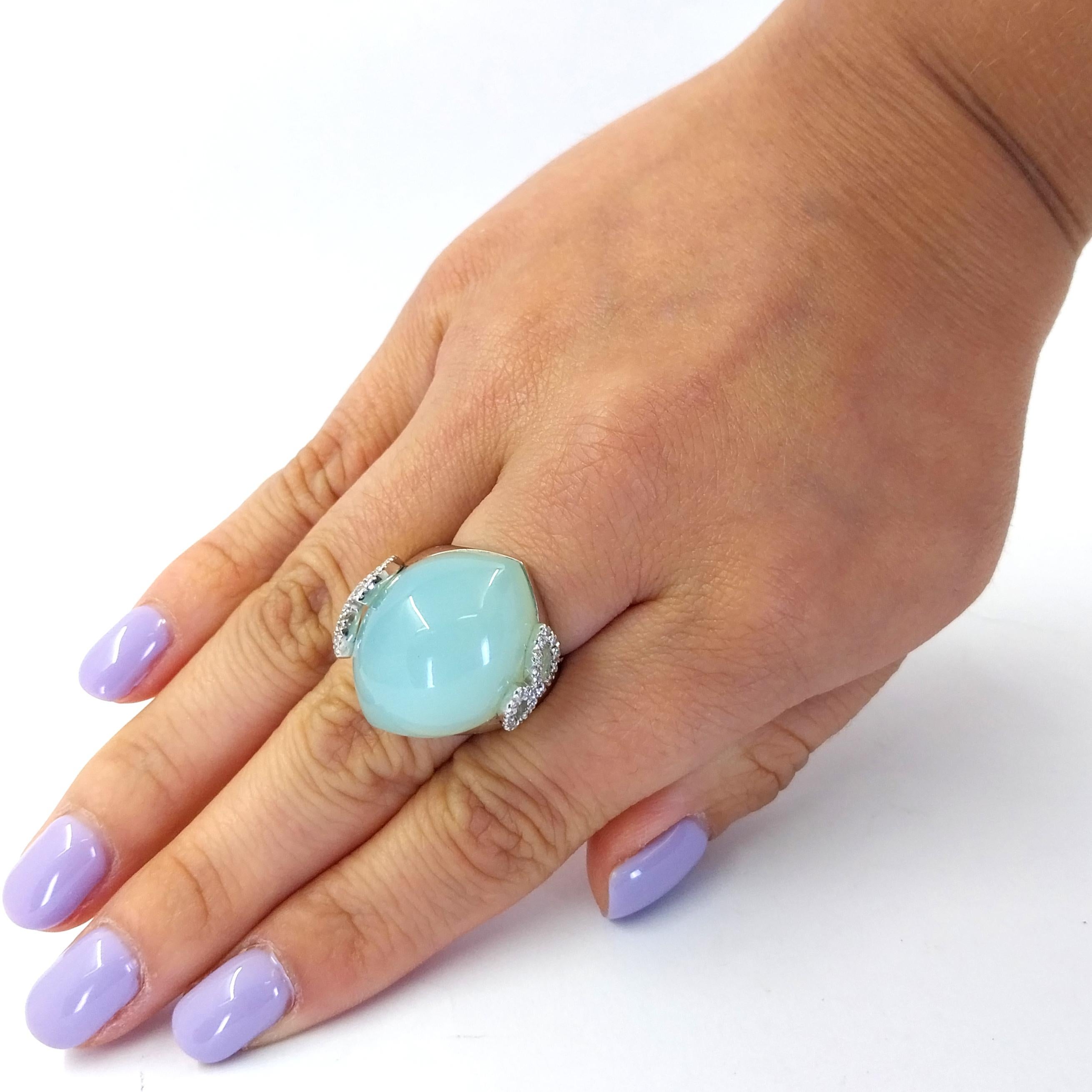 18 Karat White Gold Cocktail Ring Featuring A Cabochon Cut Blue-Green Chalcedony Measuring 24mm x 20mm Accented by 40 Round Diamonds of VS Clarity and G/H Color Totaling 0.25 Carats in a Leaf Design. Adjustable Finger Size 5.5 to 6.5 with Butterfly