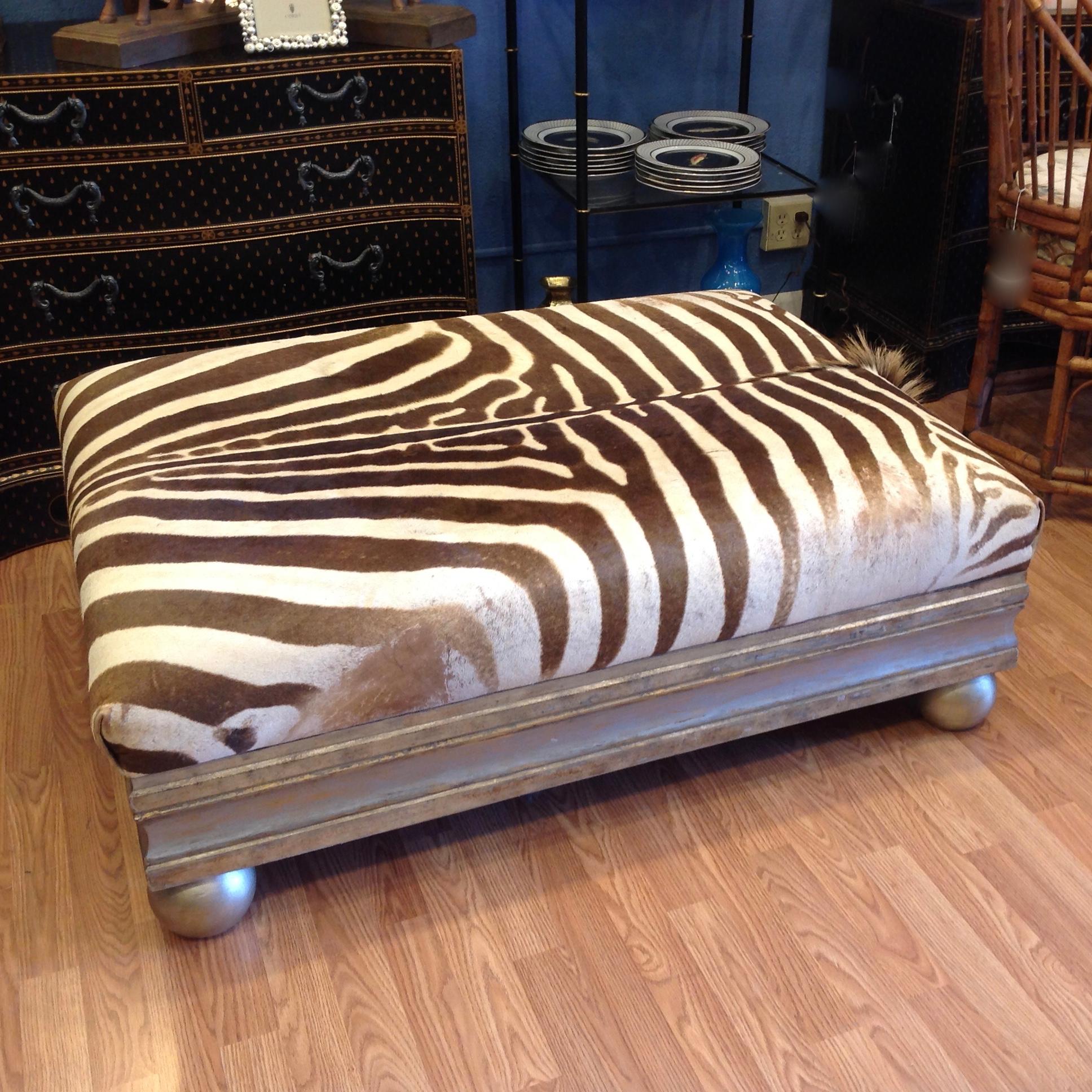 Fashioned from a complete hide sporting its mane. 
The ottoman is cocktail table height and is supported by a silver gilt wood 
trimmed base terminating in ball feet.