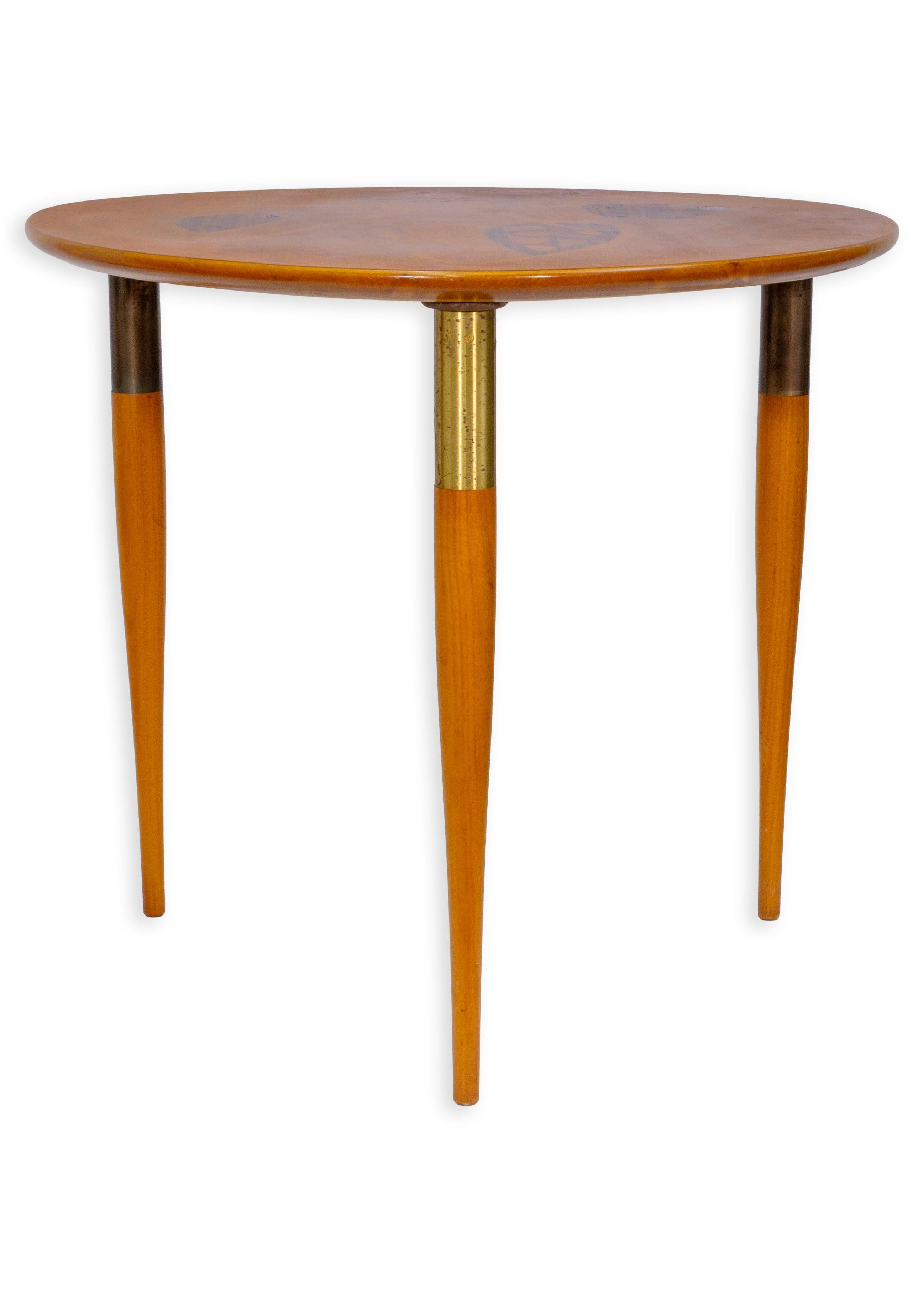 This 1953 accent table by Enro Fabry exemplifies mid-century artistry with its refined craftsmanship and abstract surface design. The round top features intricate wood inlay in geometric and organic motifs, creating a striking interplay of pattern