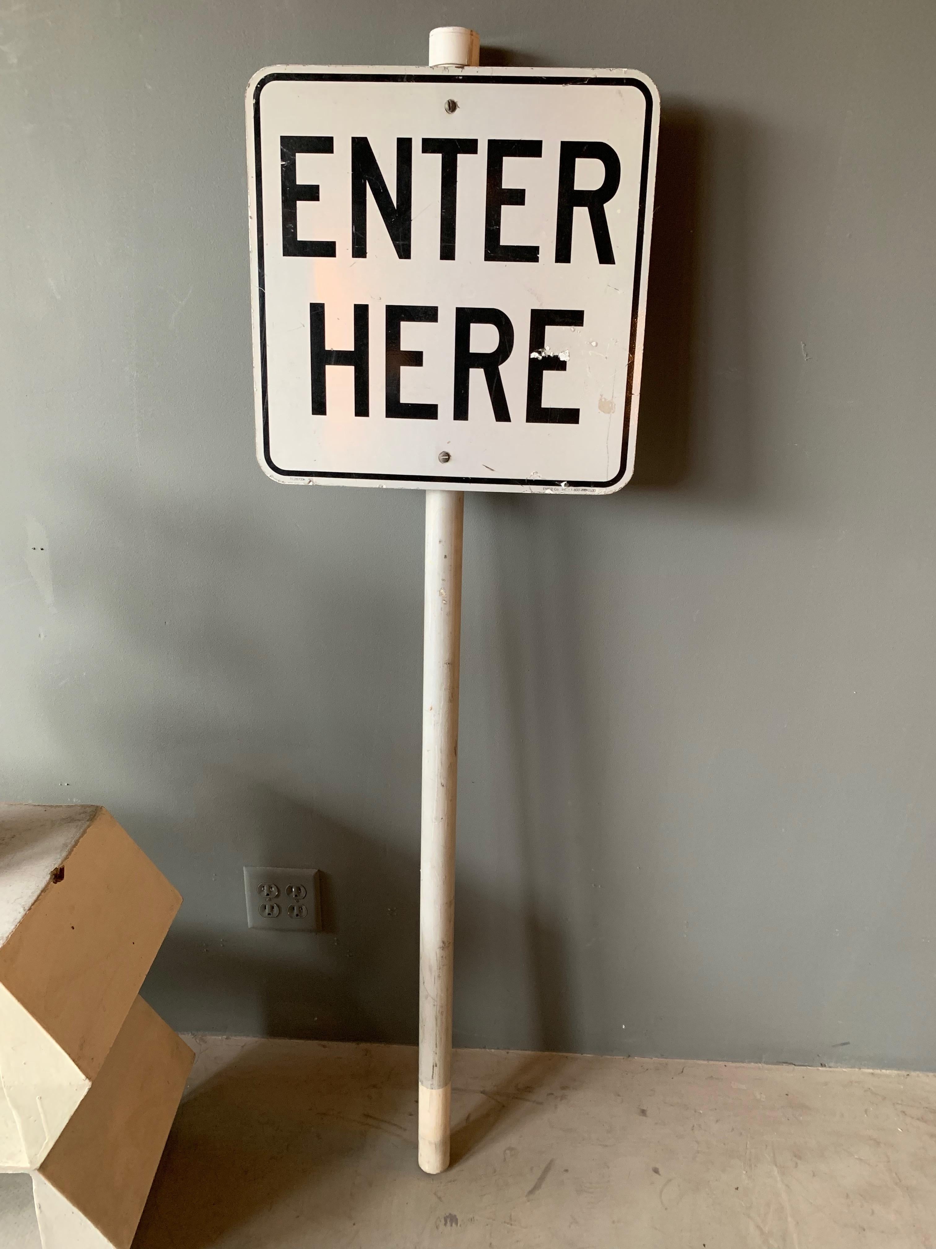 Vintage metal street sign illustrating 'Enter Here.' Sign is affixed to a pipe with reflective tape on the front. Meant to be driven into the ground. Good vintage condition.