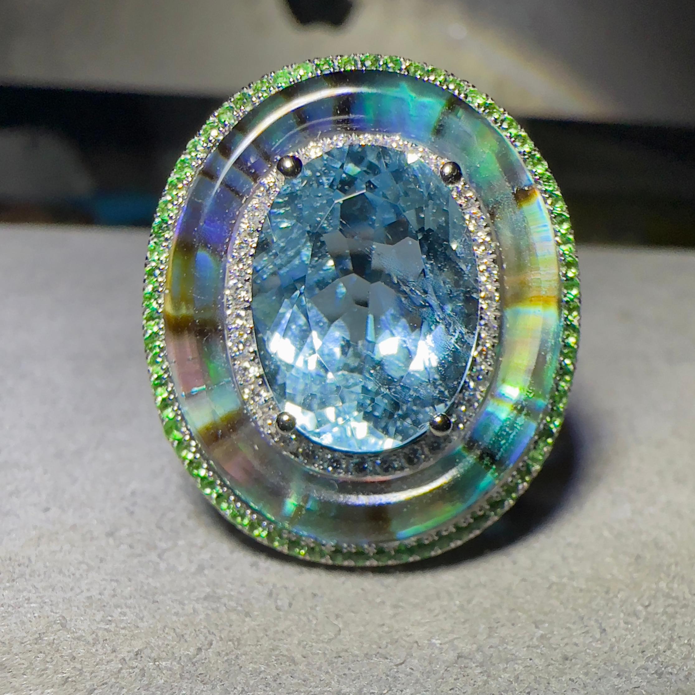 A 4.56 ct aquamarine, Tsavorite, Abalone Shell, Crystal and Diamond in 18k white Gold. The aquamarine is surrounded by a circle of diamond pave, on the outer circle is where the abalone shell is. The abalone shell is cover by thick crystal  giving