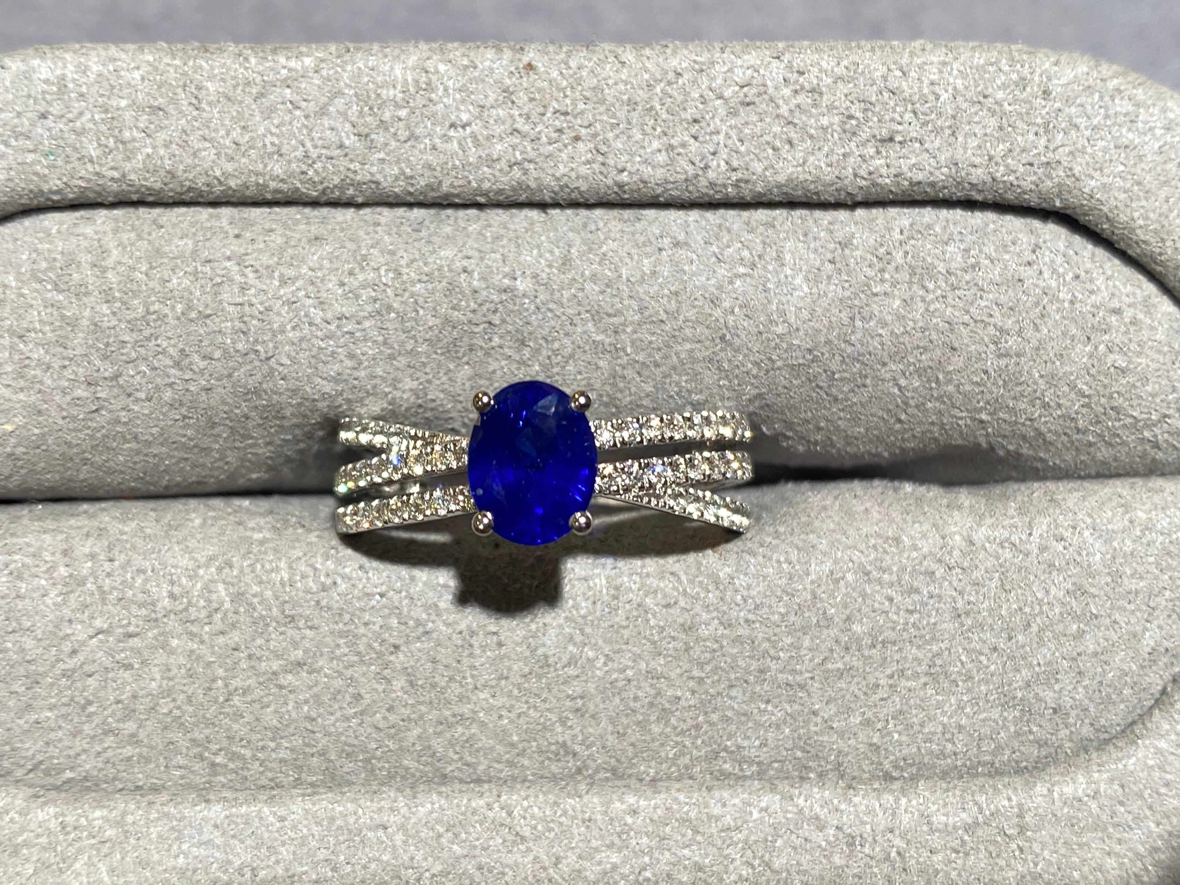 A Blue Sapphire and Diamond Ring in 18k White Gold. The main sapphire is secured by 4 white gold claws and the band of the ring is made up of 3 lines of diamond pave. Two of the diamond pave lines are parallel to each other while the the other