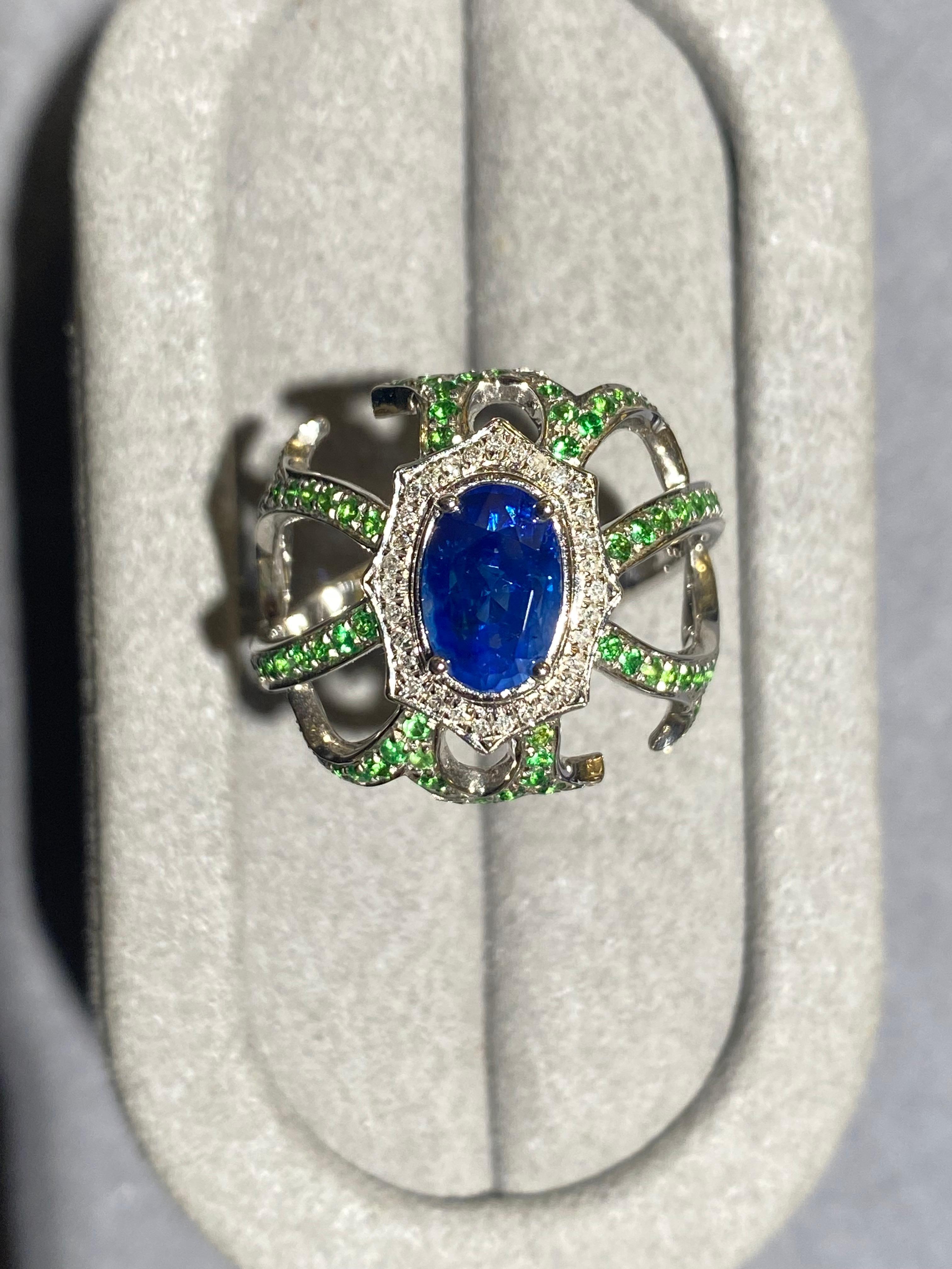 An oval shapre blue sapphire, Tsavorite and diamond ring in 18k white gold. The oval shape blue sapphire is surrounded by a circle of micro diamond pave. Several 