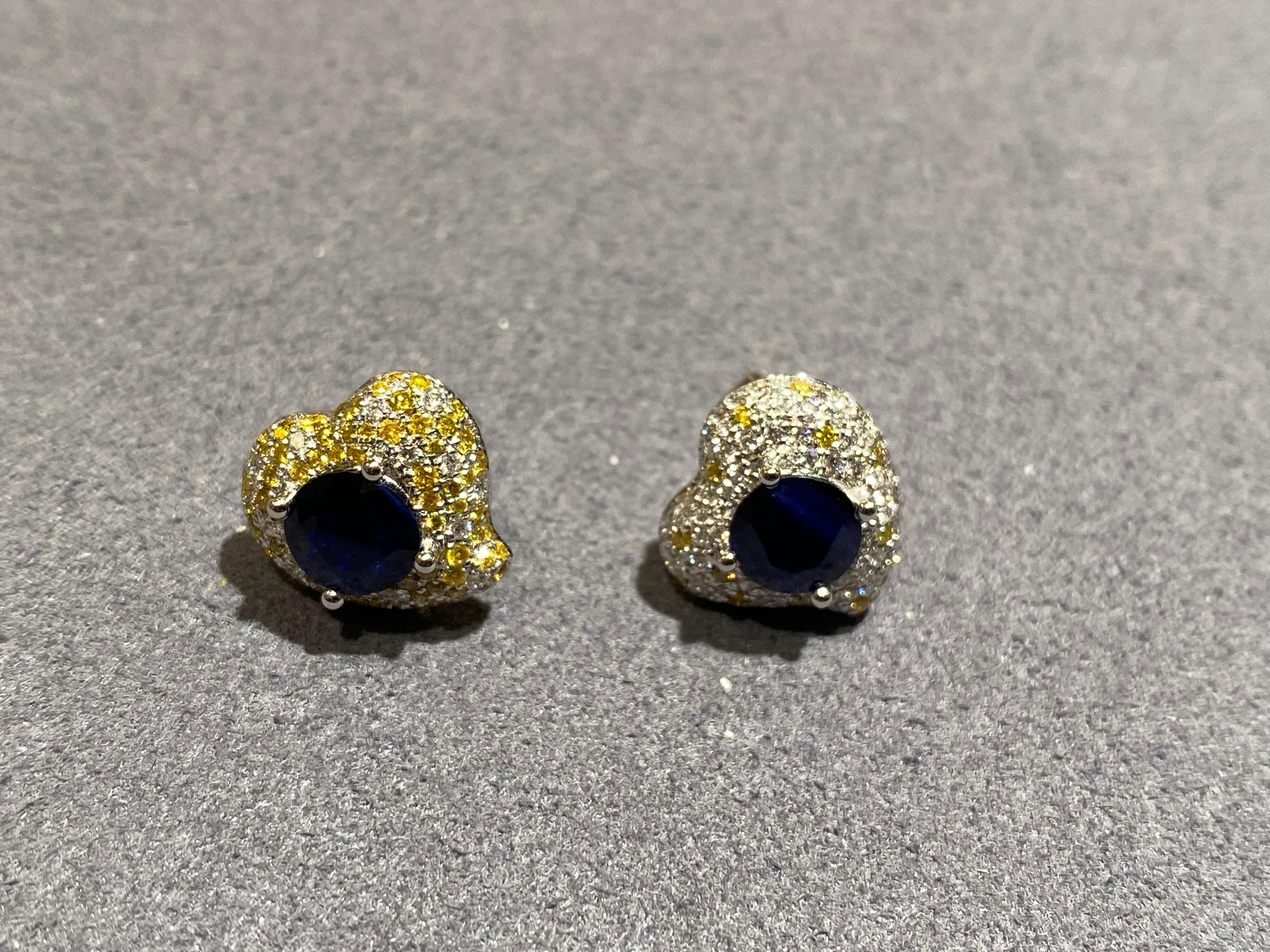 A pair of blue sapphire, yellow diamond and diamond earrings in 18k gold. It consists of 2 round brilliant cut blue sapphire set in heart shape diamond pave motif. The heart shape earring is mirror image of each other. One side of the earring is