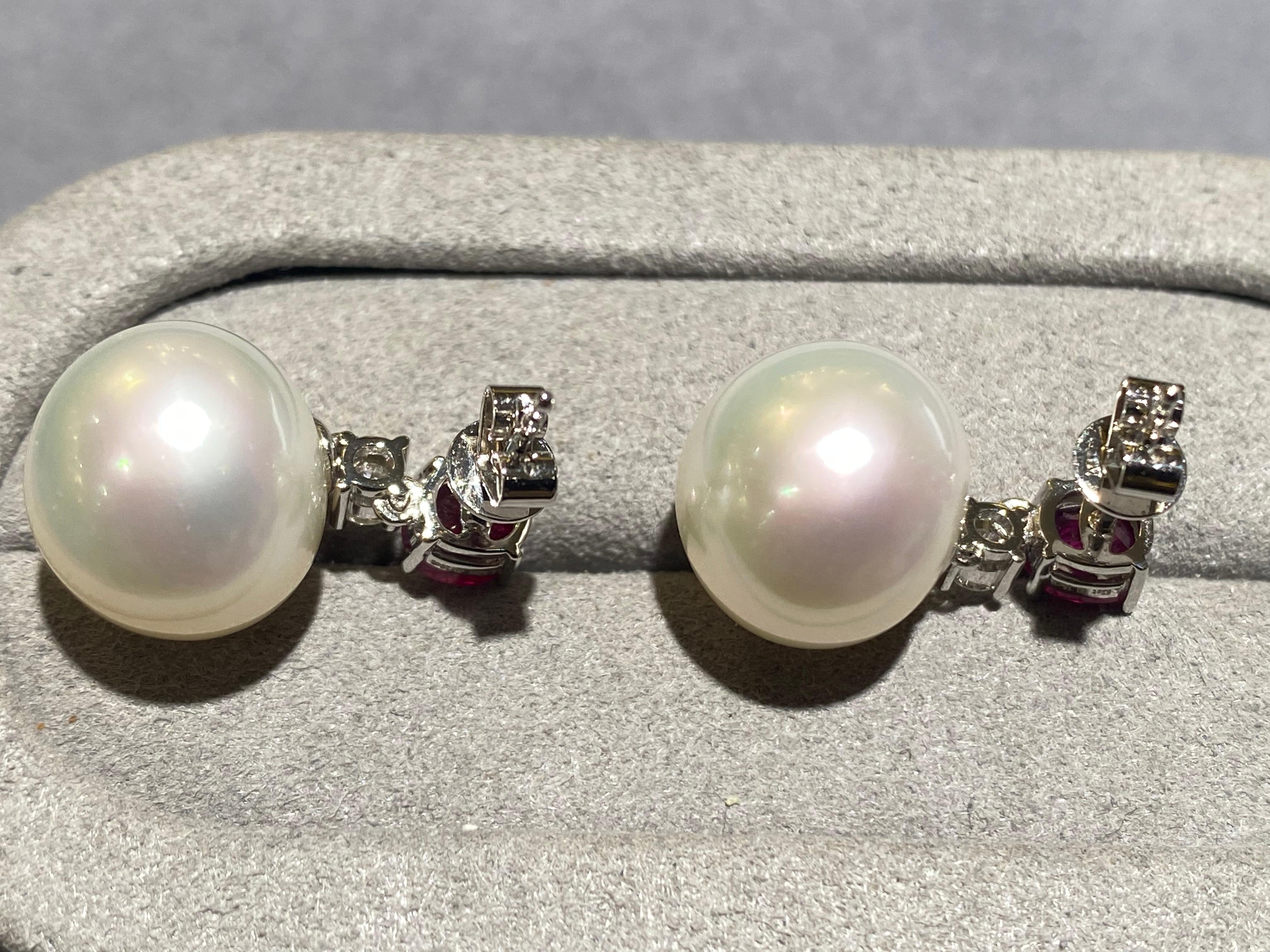 A pair of 11.5 mm x 12.5 mm button south sea pearl, ruby and diamonds earrings in 18k white gold. This dangle drop earrings is consist of a button south sea pearl hanging below the ruby ear stud connected by a brilliant cut round diamond. It is a