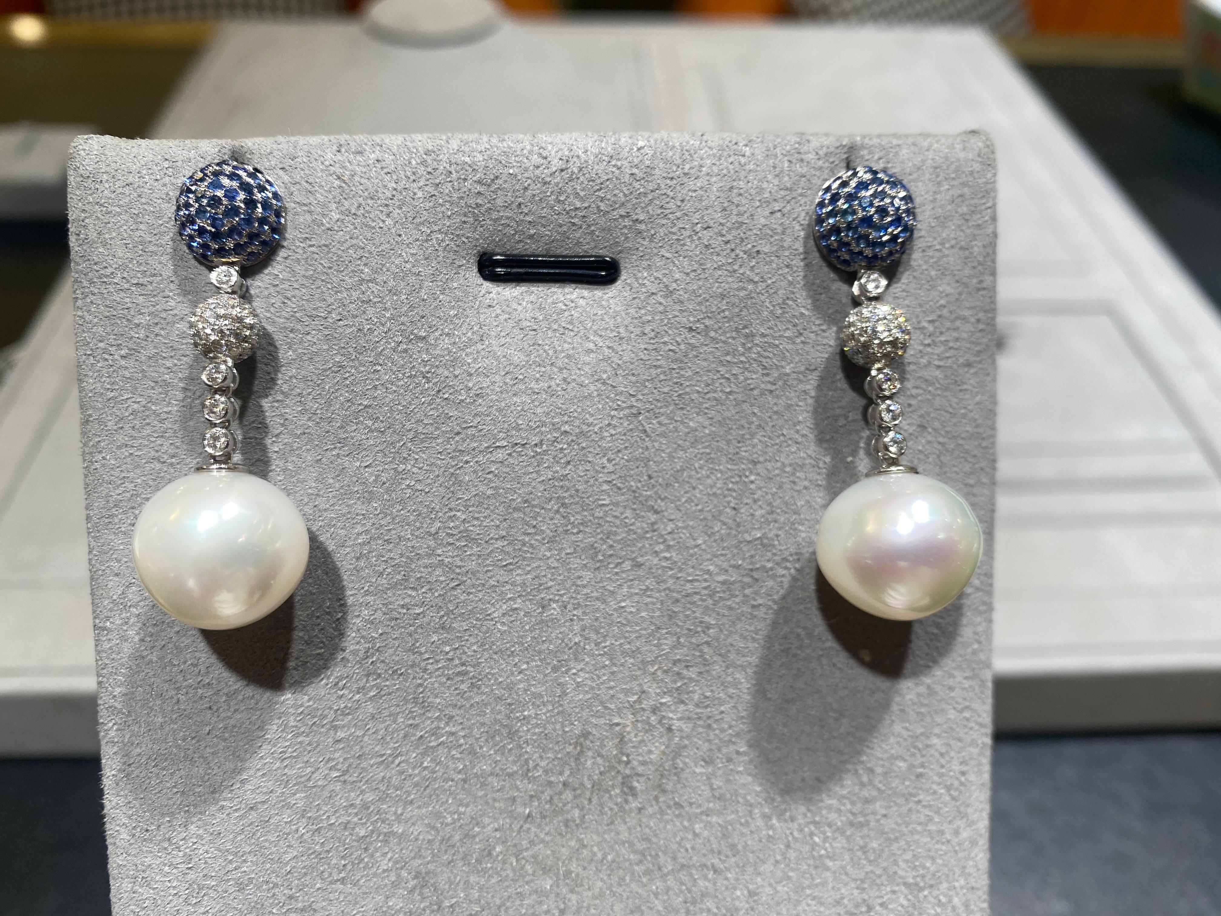 The top part of the earring is a high dome encrusted in Blue Sapphire. It is then connected by a ball full of diamond pave to the White South Sea Pearl. The Brilliant cut diamonds in between the sapphire done and South Sea Pearl add more fire and