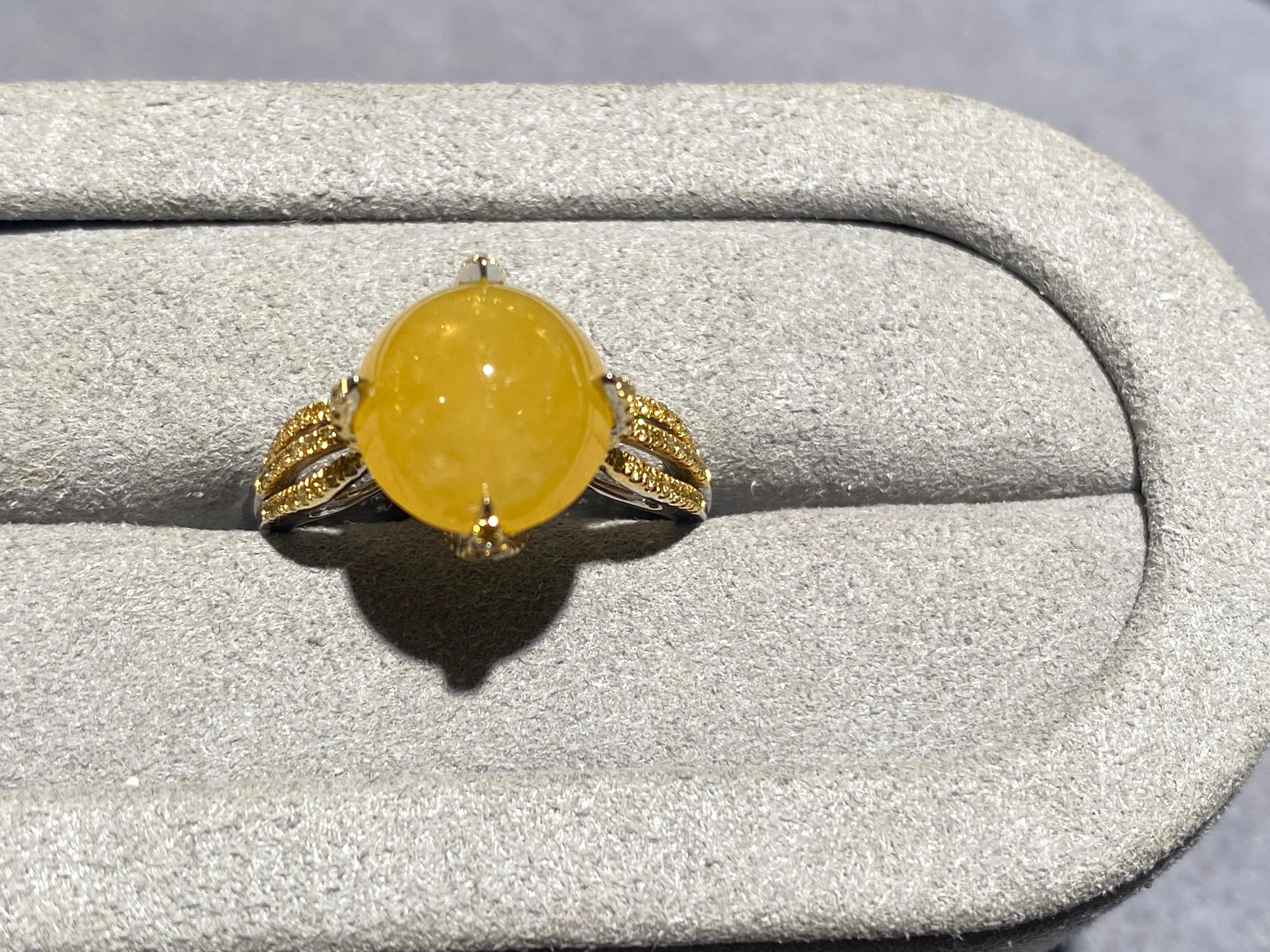 A type A yellow jadeite and diamond ring in 18k white gold. The yellow jadeite cabochon is secured by 4 big claws. Each of the claws is set with micro diamond pave. At the bottom of the jadeite, there are 2 layers of structures set with diamond