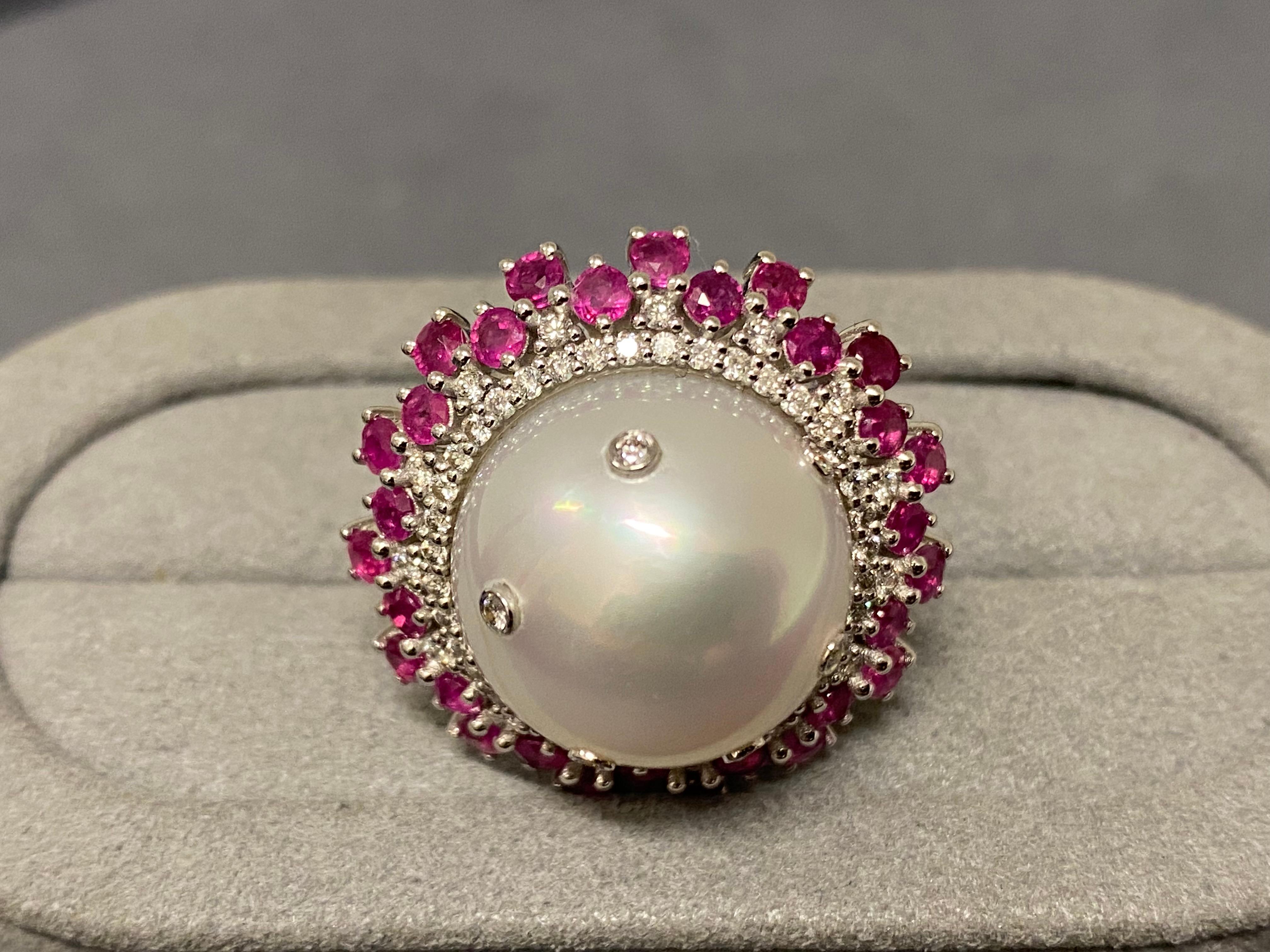 A 16.7 mm round white colour south sea pearl, ruby and diamonds ring in 18k white gold. This is a cluster ring design with diamond and ruby paves surrounding the pearl. The inner layer is the diamond pave and the next layer consists of diamond and