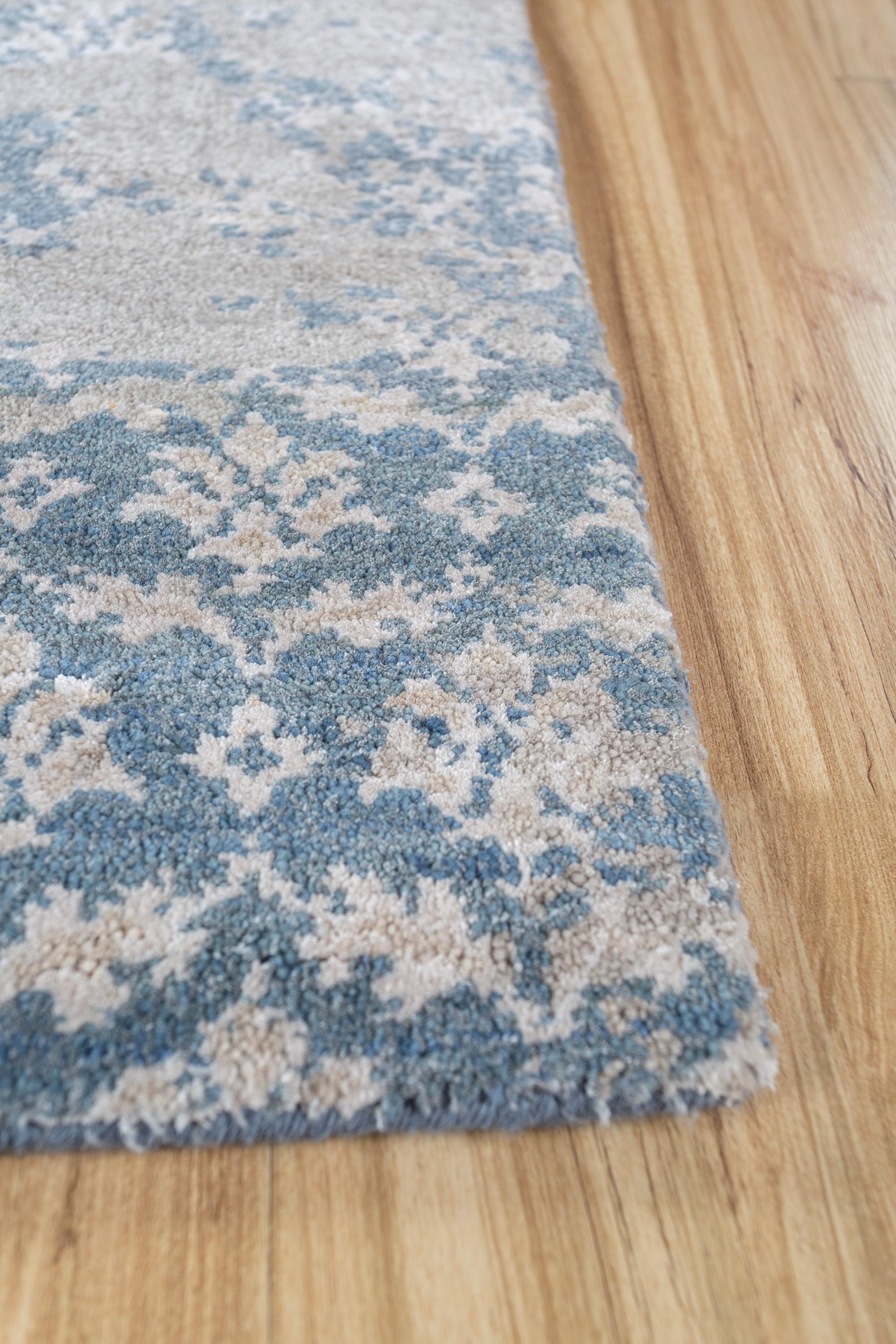 Dive into the enchanting depths of this hand-knotted rug . Its ground color, faded denim, and classic gray border create a canvas inspired by the unnoticed beauty of evolving experiences. Much like the mystery of an unfolding journey, every pattern