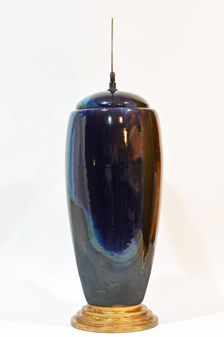 Standing 28 inches tall this lidded ceramic vase is crowned by a half moon shape multi colored iridescent (one side black) bronze handle on a hand crafted bronze mount. The vase rests on a stepped circular gold finish bronze base. The free flowing