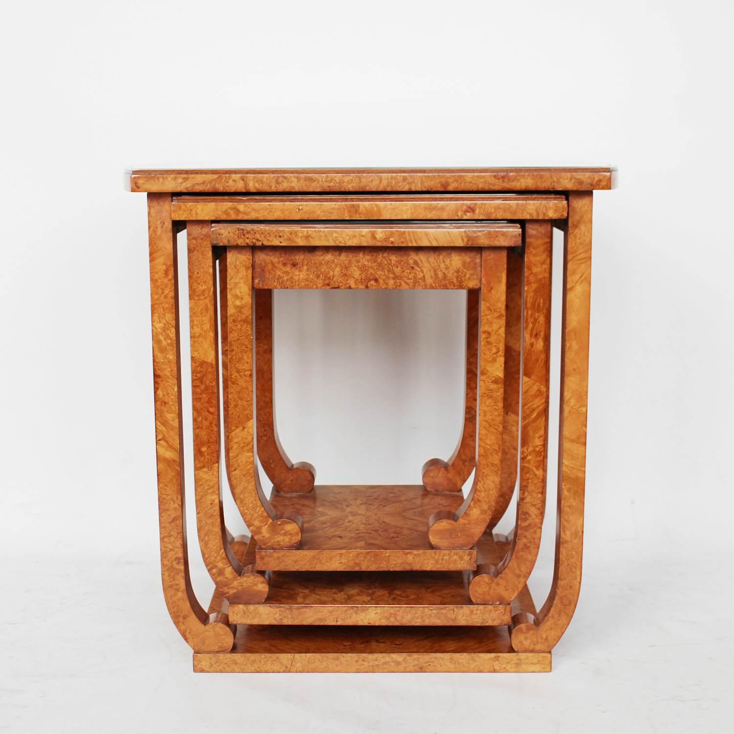 An Art Deco nest of hanging side tables with inset glass tops. Set over legs with scrolled feet on squared bases. Burr walnut throughout. 

Dimensions: H 56.5 cm, W 56.5 cm, D 38 cm, H 47.5 cm, W 41 cm, D 34.5 cm, H 38.5 cm, W 32.5 cm, D 30 cm.


