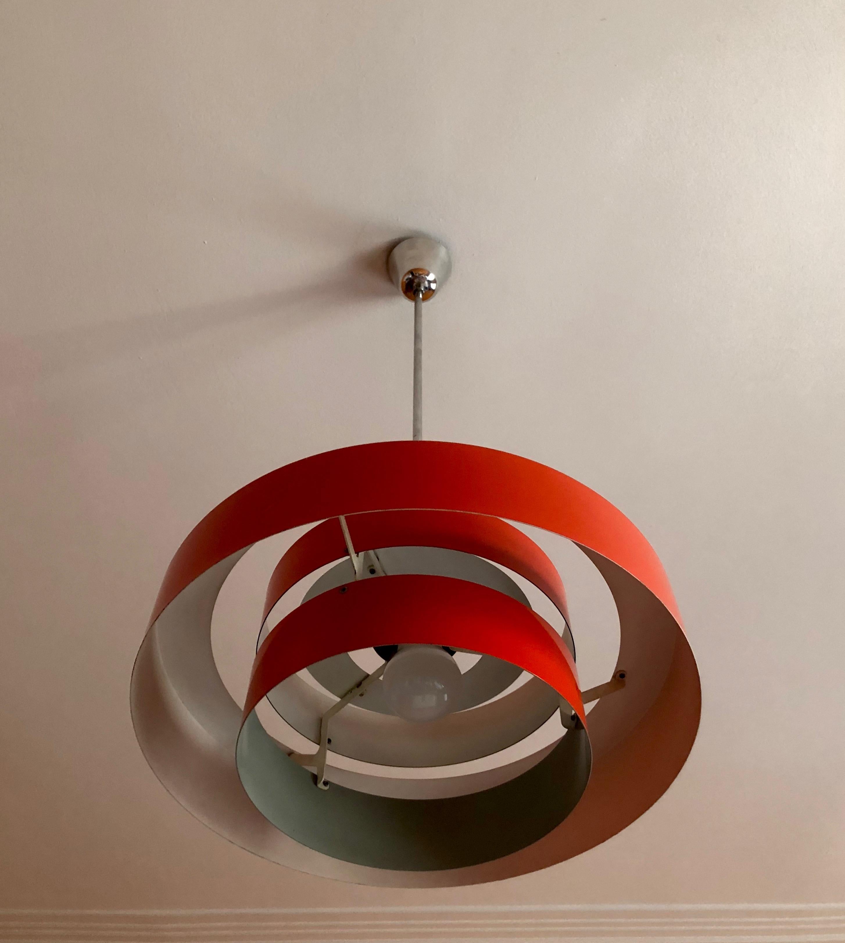 The equator, is a bright red pendant lamp, with a Space Age design. It is composed of two inner rings surrounded by a larger outer ring and a cylinder top. The rings have a white inner coating with the bottom ring featuring a grey coating, that acts