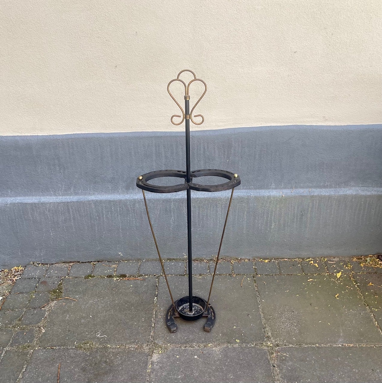 Equestrian themed umbrella stand made from 3 black horseshoes, brass string sides, a small aluminium base and topped with a brass ornament. This piece in original condition dates from the 1930s and it was made in Denmark. Measurements: H: 90 cm, W: