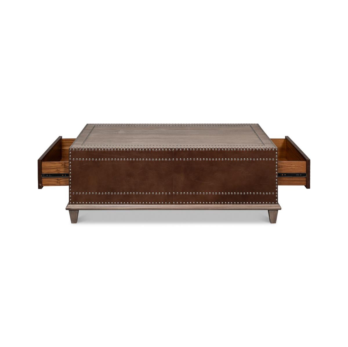 Une table basse classique d'inspiration équestre avec des côtés enveloppés de cuir marron. Avec des accents de têtes de clous placés à la main et deux grands tiroirs à chaque extrémité. Surélevée sur une base en bois gris.

Dimensions : 50