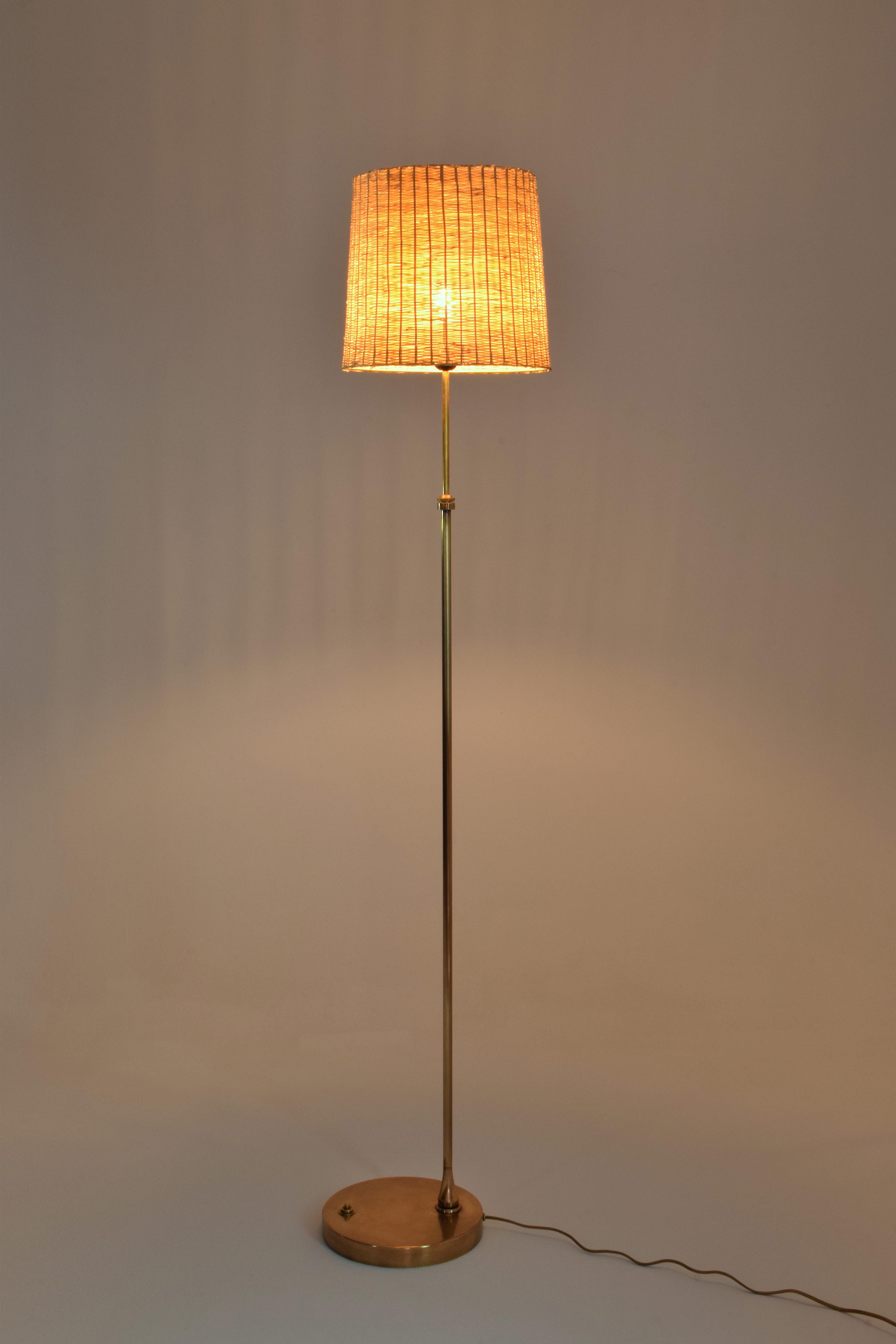 The Ancora-P floor light stands on a slender brass structure and a sophisticated disk base. The shade is delicately handcrafted by expert Moroccan artisans in wicker and features a leather braided detail. This fantastic piece is pictured here in an