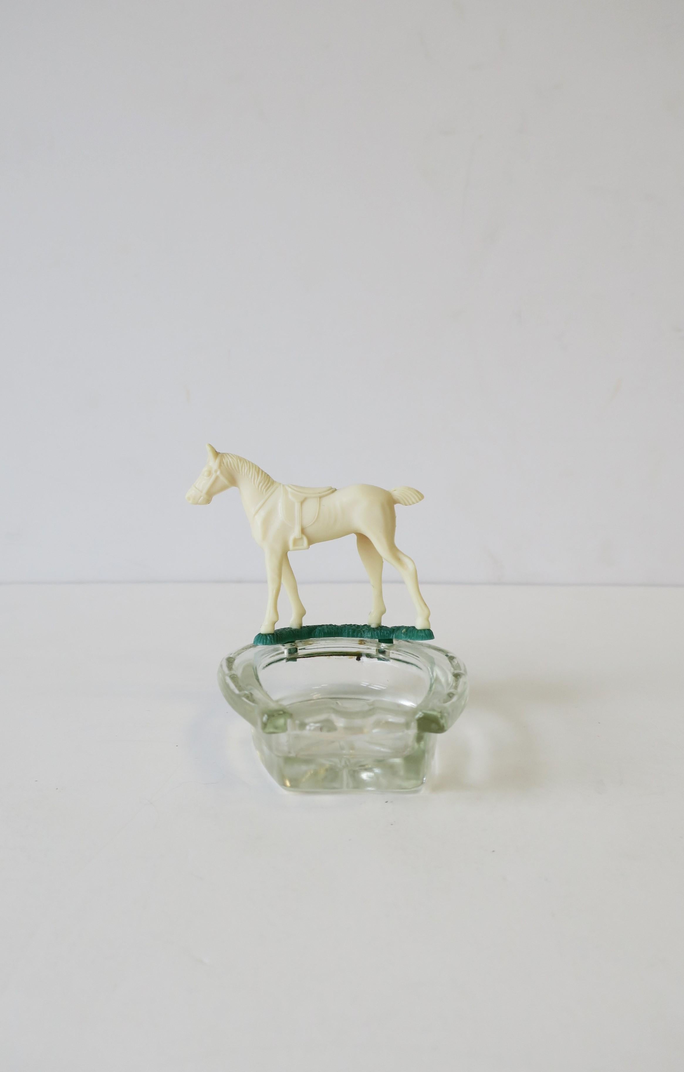 An small equine horse and horseshoe trinket jewelry dish ashtray, circa early 20th century, USA. This beautiful white resin horse, with green grass under hoofs, sits atop a cut glass horseshoe shaped ashtray. Small indent to hold cigarette. Nice