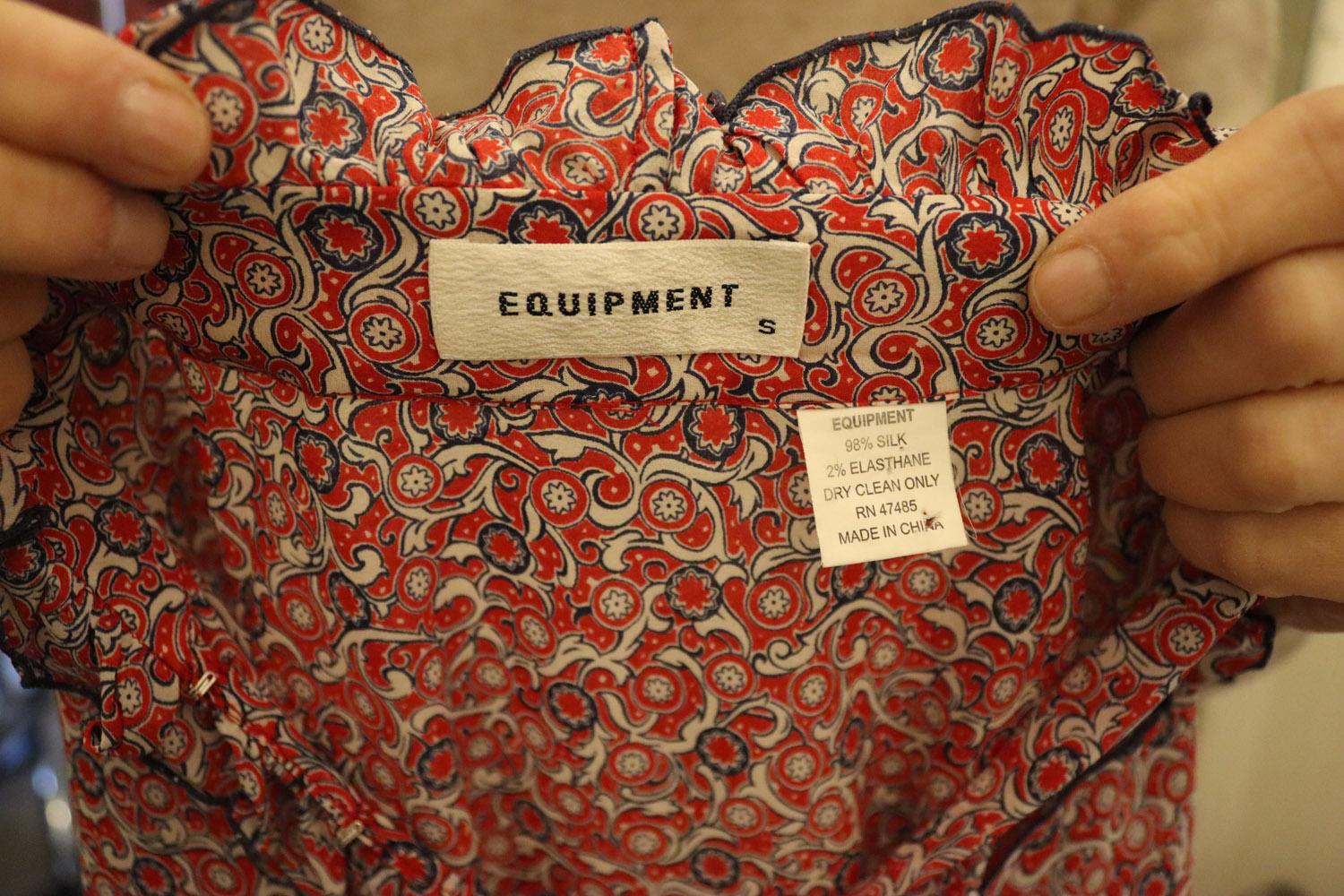 Un joli chemisier en soie de la marque Equipment.  Dans un joli imprimé rouge, blanc et bleu, le chemisier est sans manches et présente des détails à volants sur le devant et le col. Le jabot est bordé de bleu et la blouse se ferme par des crochets