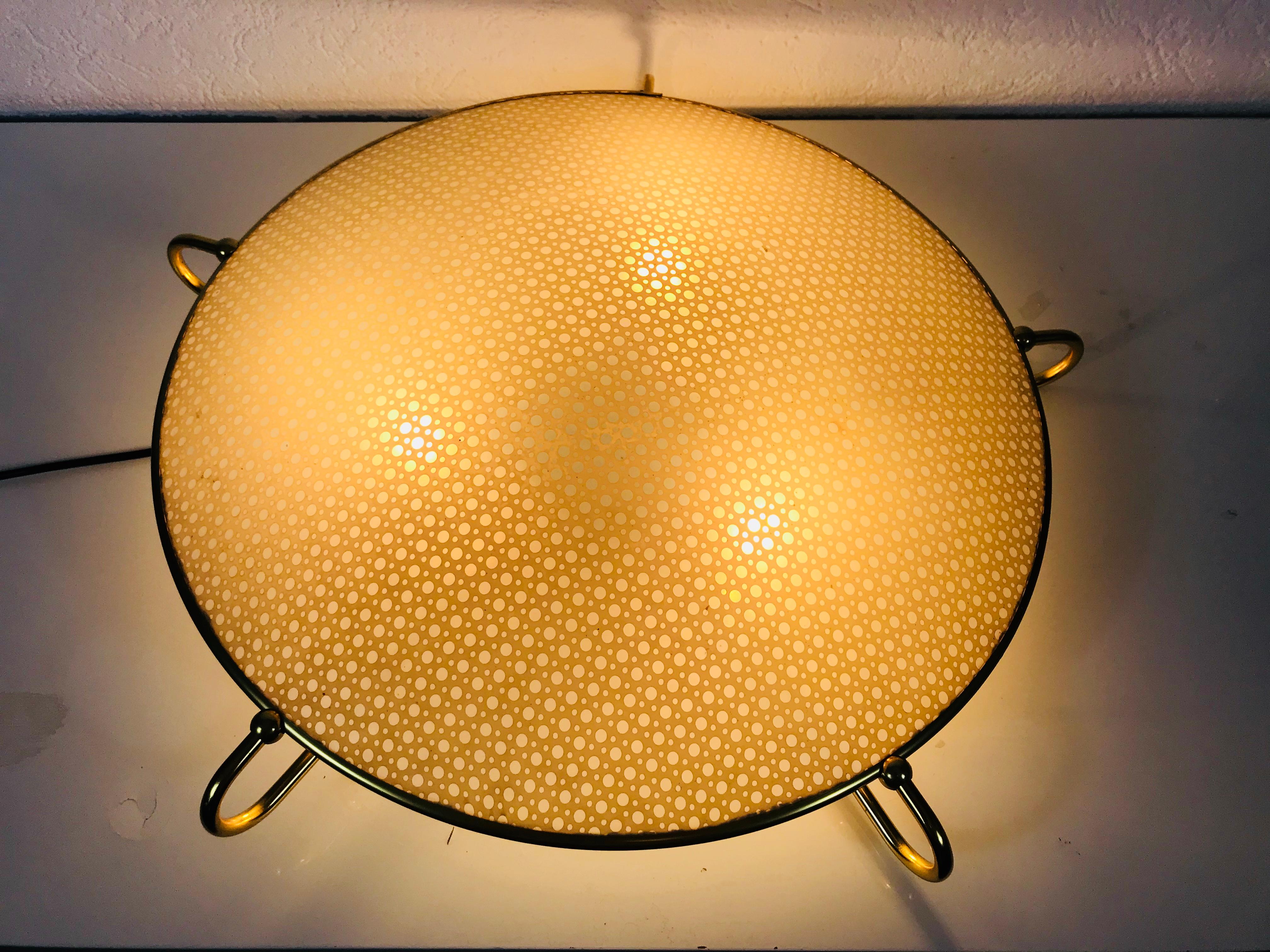 A midcentury flush mount made in Germany in the 1960s. It is fascinating with its rare plastic shade which is surrounded by a brass frame. The shade is arched outside. The sockets are made of Bakelite.

The light requires E27 light bulbs.