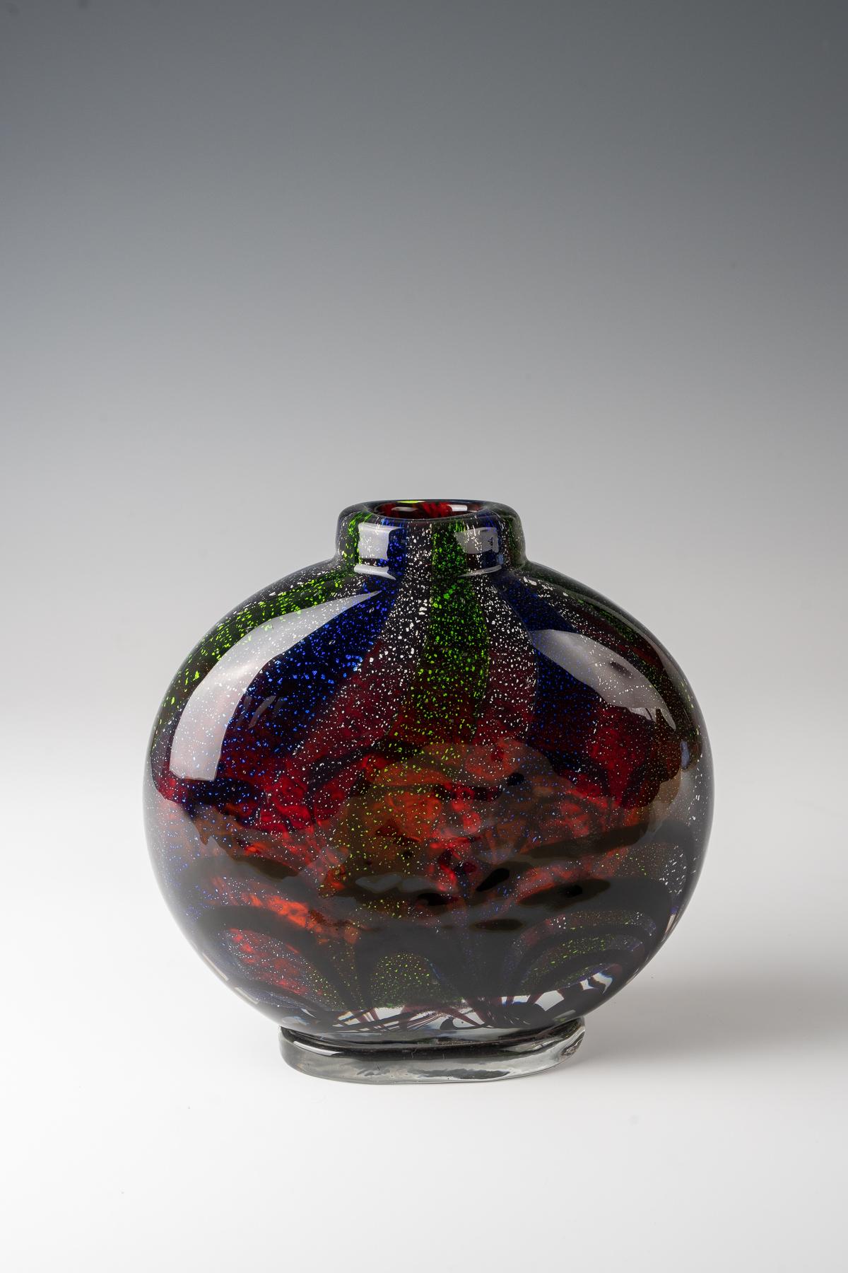 Ercole Barovier (1889-1974), vaso in vetro 'Oriente', 1940 ca.
vaso bulboso pressato di vetro incolore a pareti spesse, nello strato intermedio si alternano bande di colore verde e blu e lamina d'argento strappata davanti a un fondo rosso
prodotto