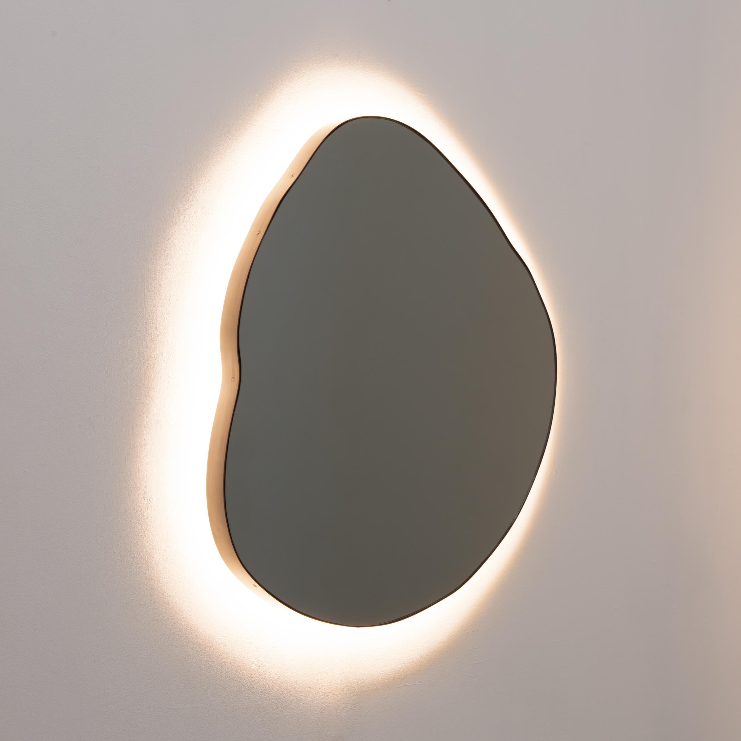 Playful and modern organic shaped back illuminated black tinted mirror with a dark patina brass frame.

All mirrors are fitted with an ingenious French cleat (split batten) system so they may hang flush with the wall in four alternative