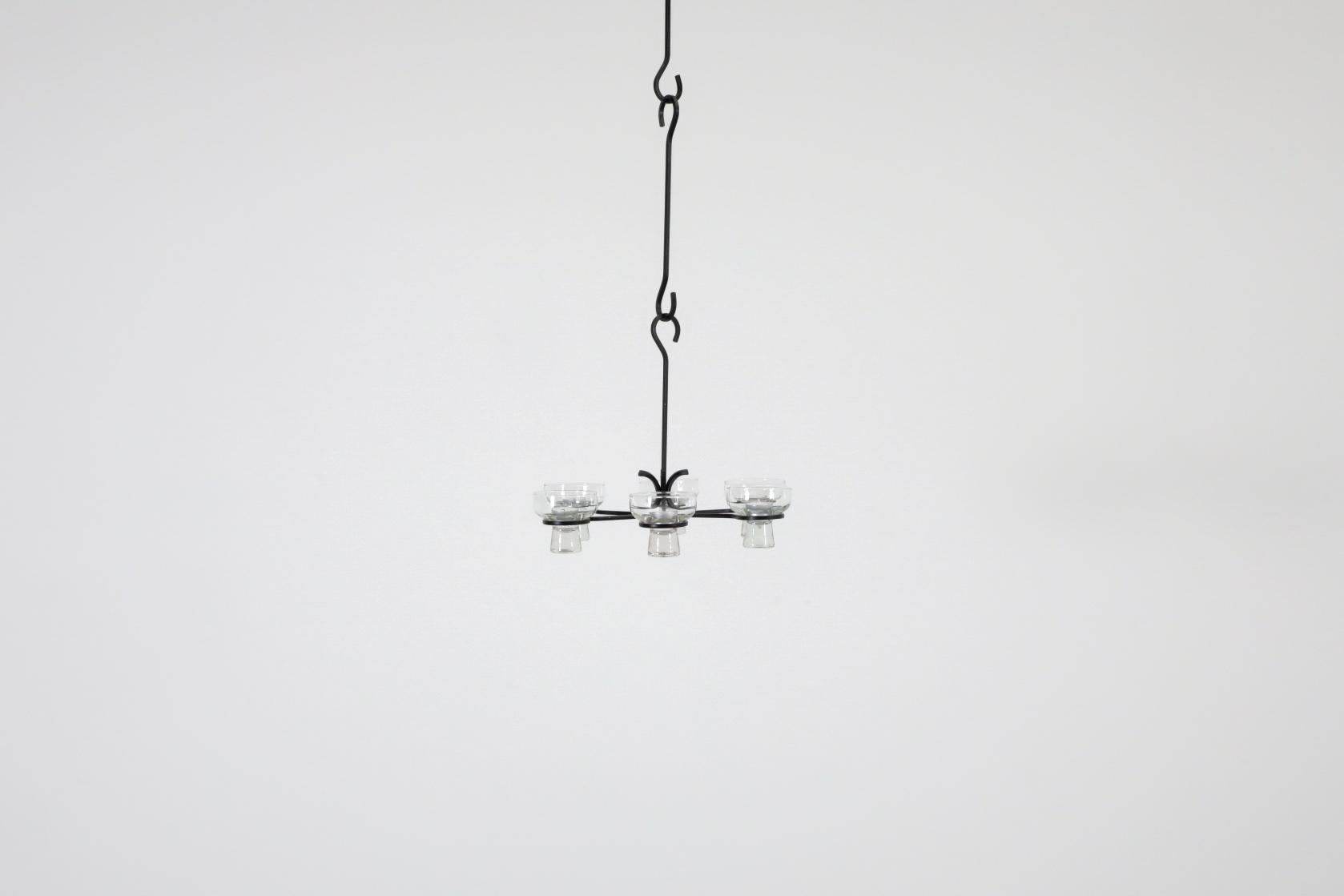Classic Swedish Mid-Century, suspended black wrought iron votive candelabra with 6 glass cups and multiple links. The piece's lines share strong similarities to the work of acclaimed Swedish design greats Eric Hoglund and Amie Stålkrantz Lundqvist.