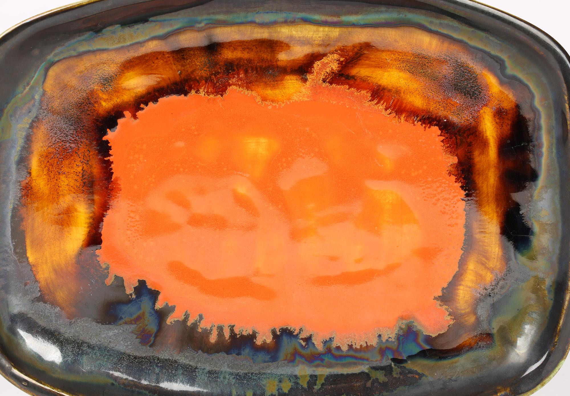 A stylish studio pottery tray or shallow dish decorated in bright orange glazes by Eric Leaper, Newlyn and dating from around 1960. The pottery tray is of rectangular shape with slightly rounded and raised sides and is decorated in layered glazes in