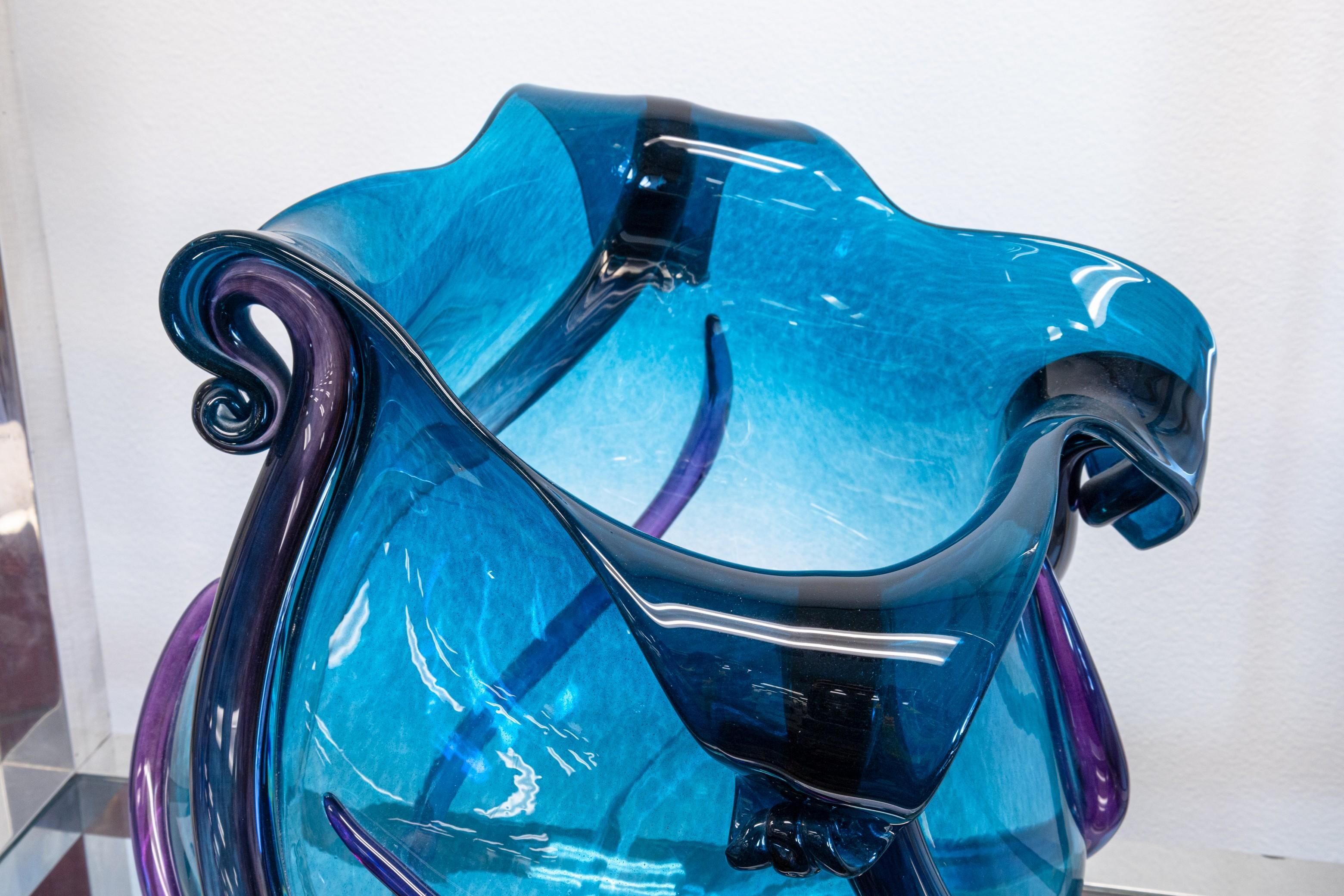 An Eric Lieberman blown glass vessel. A very pretty hand blown glass piece featuring a gorgeous combination of blues and purples with swirling strips of glass and curled rims. This piece is signed and dated 1997 on the base. It is in very good