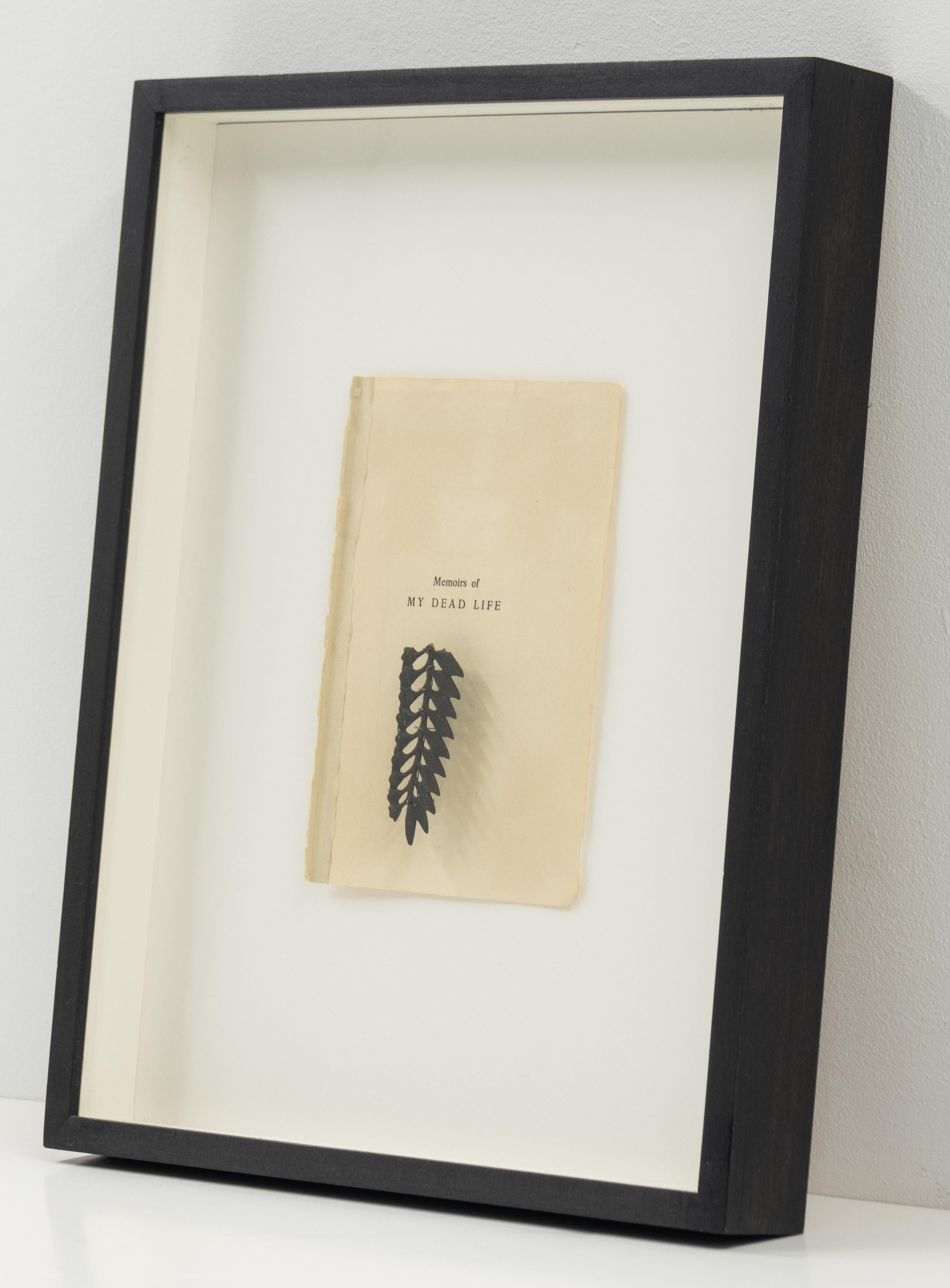 La imagen muestra una página vieja y desgastada titulada Memorias de mi vida muerta. Debajo del título hay un pequeño elemento botánico negro, parecido a una hoja o helecho prensado o tallado, pegado a la página.

Memorias de mi vida