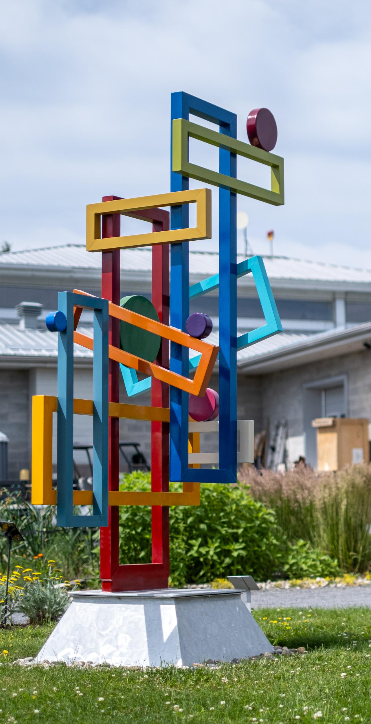 Quebec artist Éric Tardif’s colourful and engaging abstract sculptures invite the viewer to think about their own relationship to the environment. This contemporary geometric outdoor piece is forged from aluminum and painted in a crayon box of