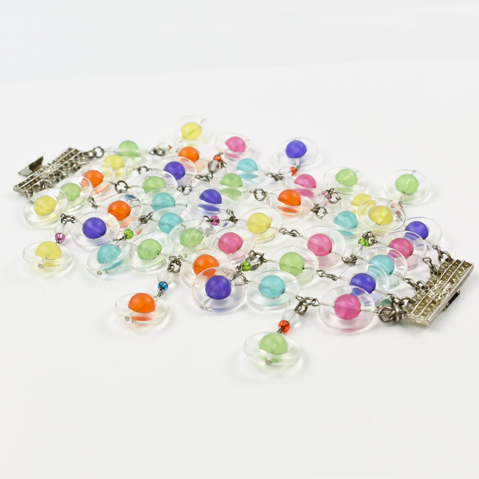 Erickson Beamon hat dieses schöne, übergroße Gliederarmband entworfen. Das Gliederdesign hat baumelnde Charms in Form eines Saturns aus Harz oder Lucite in verschiedenen Farben. Eine perfekte Kombination aus rosa, lila, grün, gelb, blau und orange.