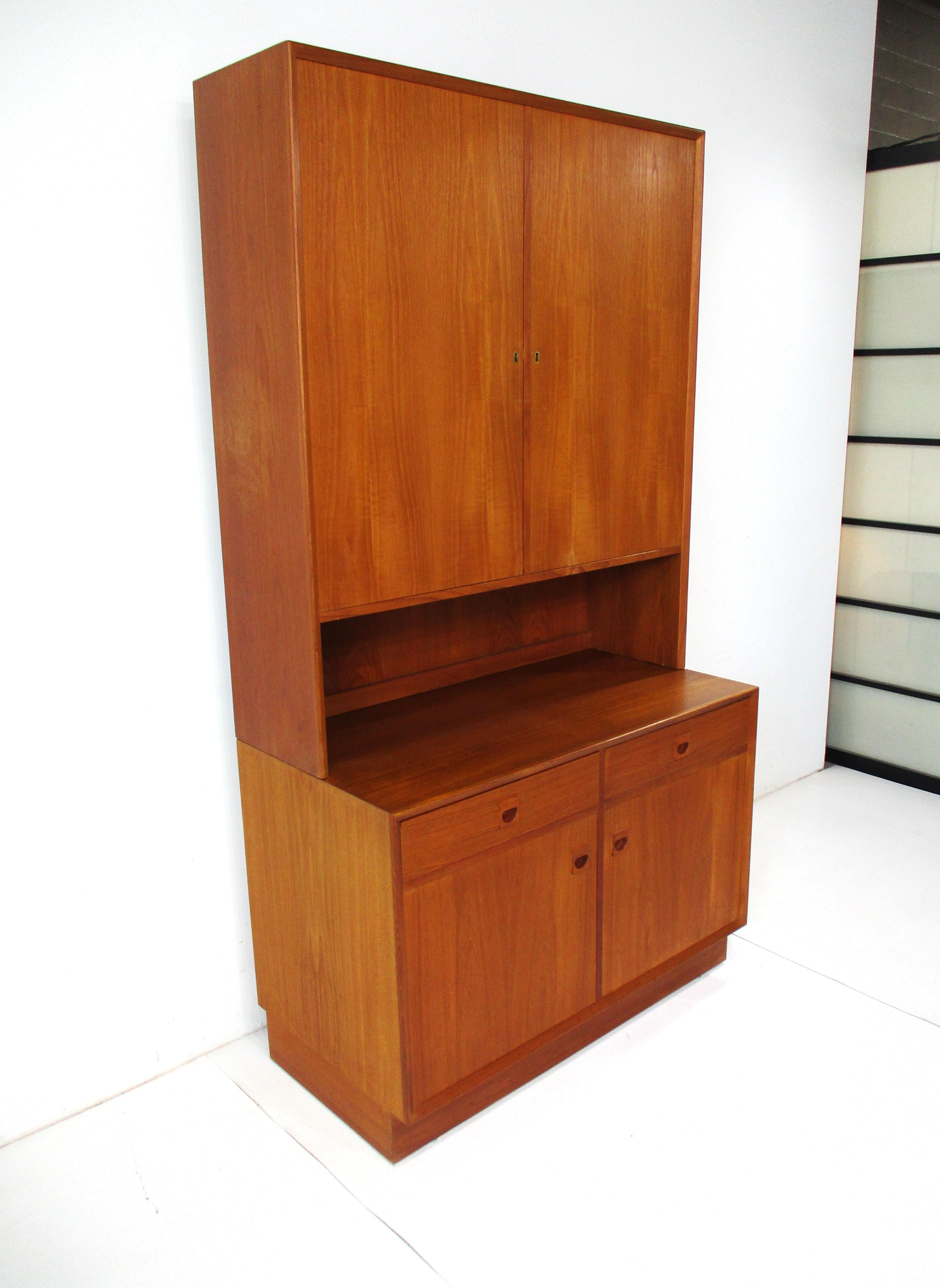 Una cassettiera in legno di teak di ottima fattura, composta da due armadietti a due ante con chiusura superiore e quattro ripiani regolabili per l'archiviazione e ferramenta in ottone. La cassettiera inferiore ha due cassetti e due ante con due
