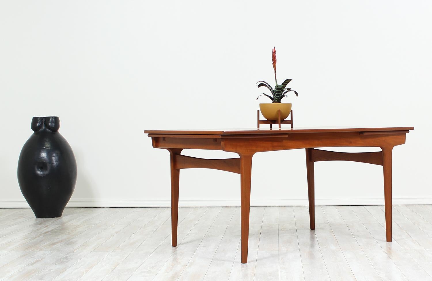 Expandable dining table designed by Erik Buch for Funder-Schmidt & Madsen in Denmark circa 1960’s. This elegant table features a teak wood frame with tapered legs supported by bow-shape support stretchers. The top feature two extendable leaves that