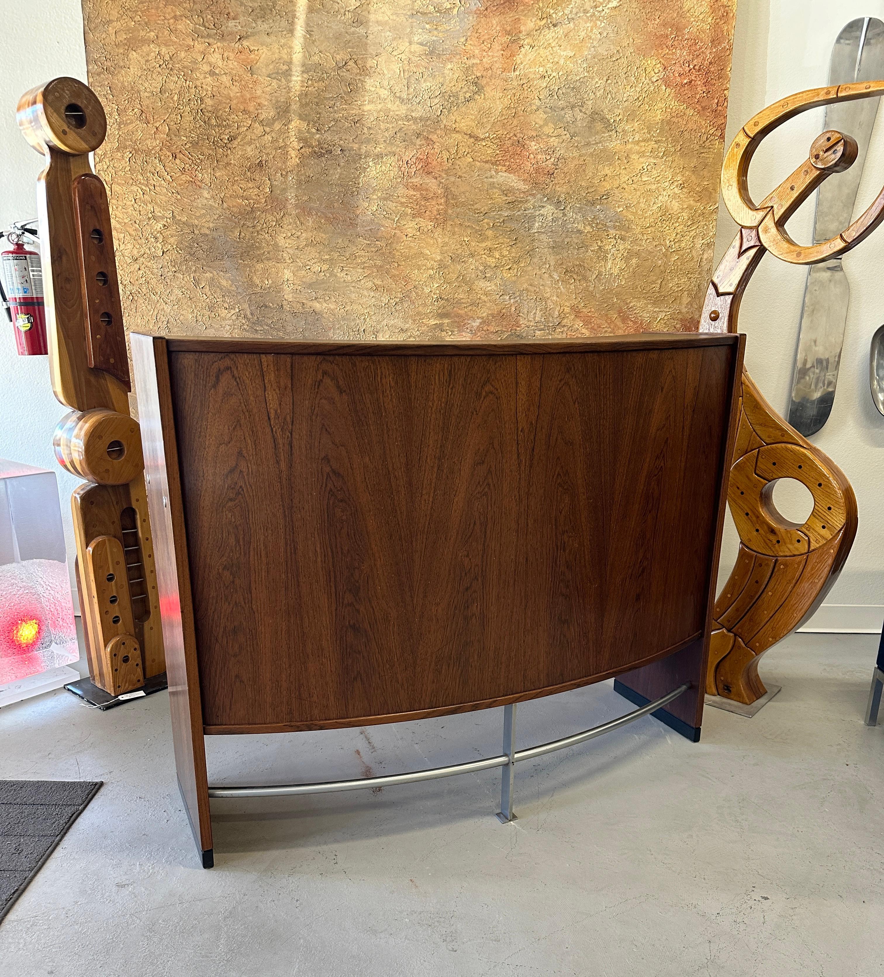 A lovely rosewood bar by designed by Erik Buch for Drylund. Features bottle hole compartments, 2 drawers and sliding doors. Curved front with a metal rail or footrest on the bottom. In good age appropriate condition with some minor marks to the
