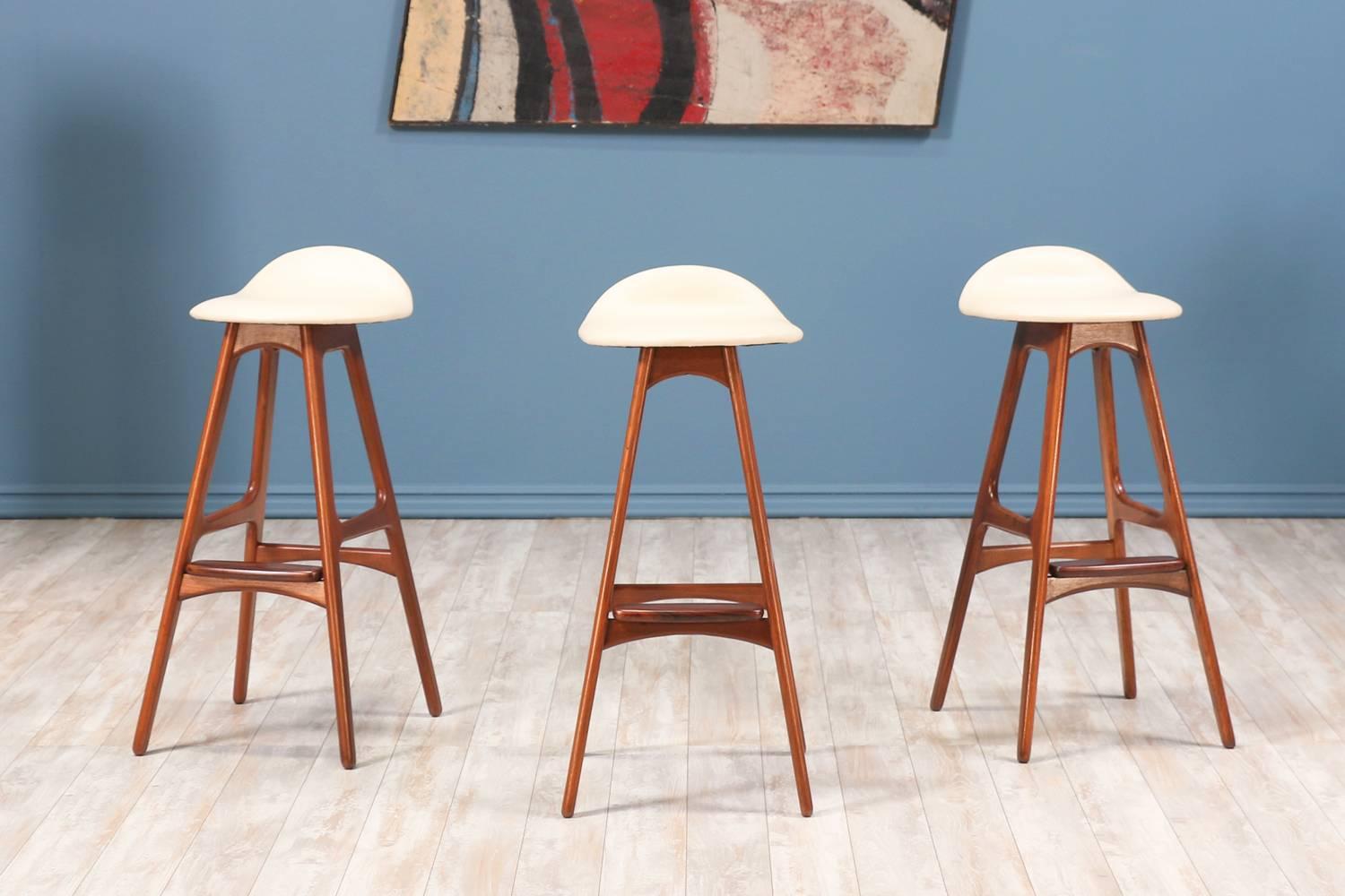 Set of three model 61 bar stools designed by Erik Buch for Oddense Maskinsnedkeri and manufactured in Denmark circa 1960’s. Each stool features a streamline design with a solid teak wood frame, gorgeous contrasting rosewood footrest and a sculpted
