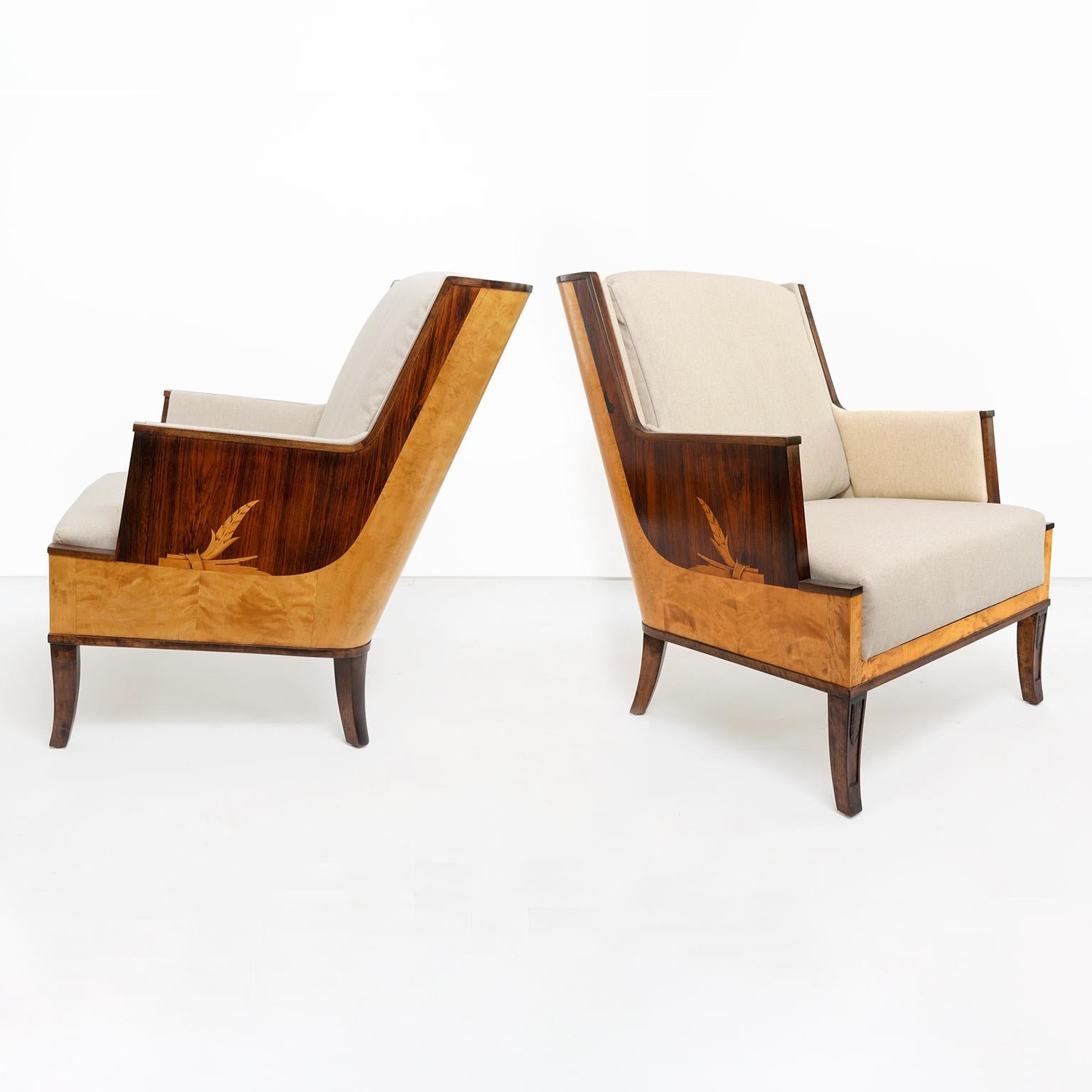 Elegant pair of Swedish art deco armchairs / lounge chairs designed by Erik Chambert. Chairs feature a sleek wood veneered frame in rosewood and birch veneer and a beautifully rendered marquetry design on each side. Angular arms create a modern
