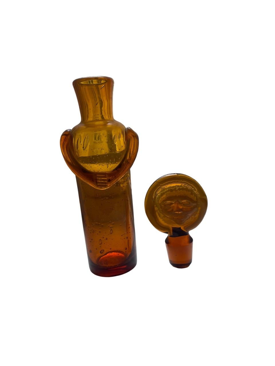 A rare and sculptural art glass bottle by renowned Swedish designer Erik Höglund, created for Boda Glasbruk in the 1950s. This handmade piece features a distinctive figural stopper with a pressed face motif—an iconic and highly collectible element