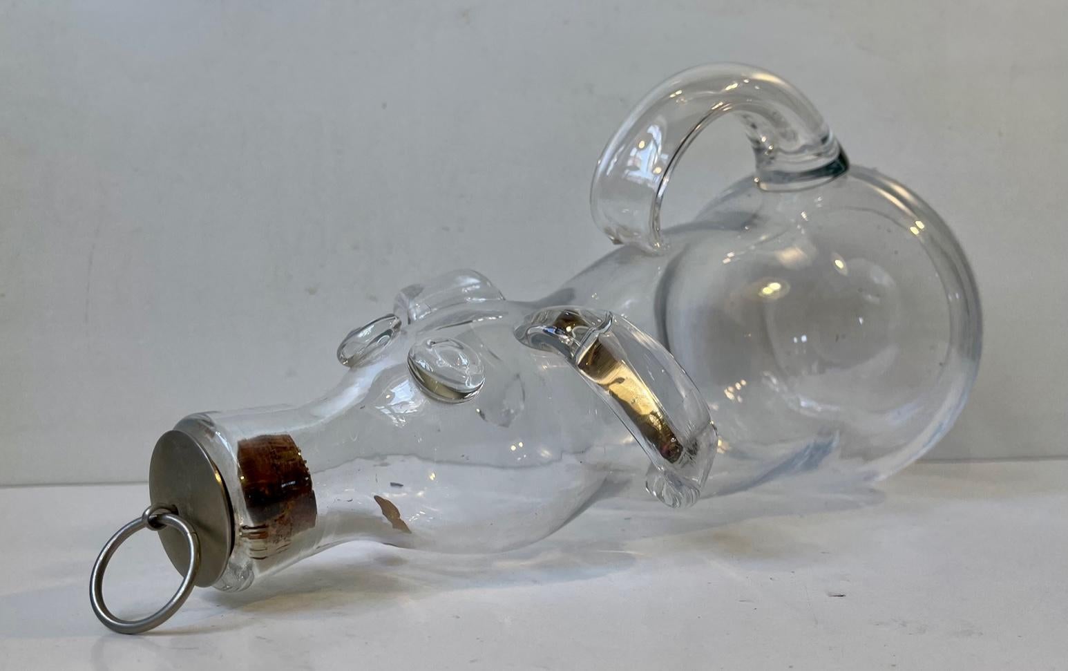 Humorous decanter with handle depicting a dog or pig. Studio-made in Hand-blown clear glass. Designed by Erik Höglund and manufactured by Boda in Sweden circa 1970-75. Label from Boda still present to the side. Measurements: height: 30 cm, diameter: