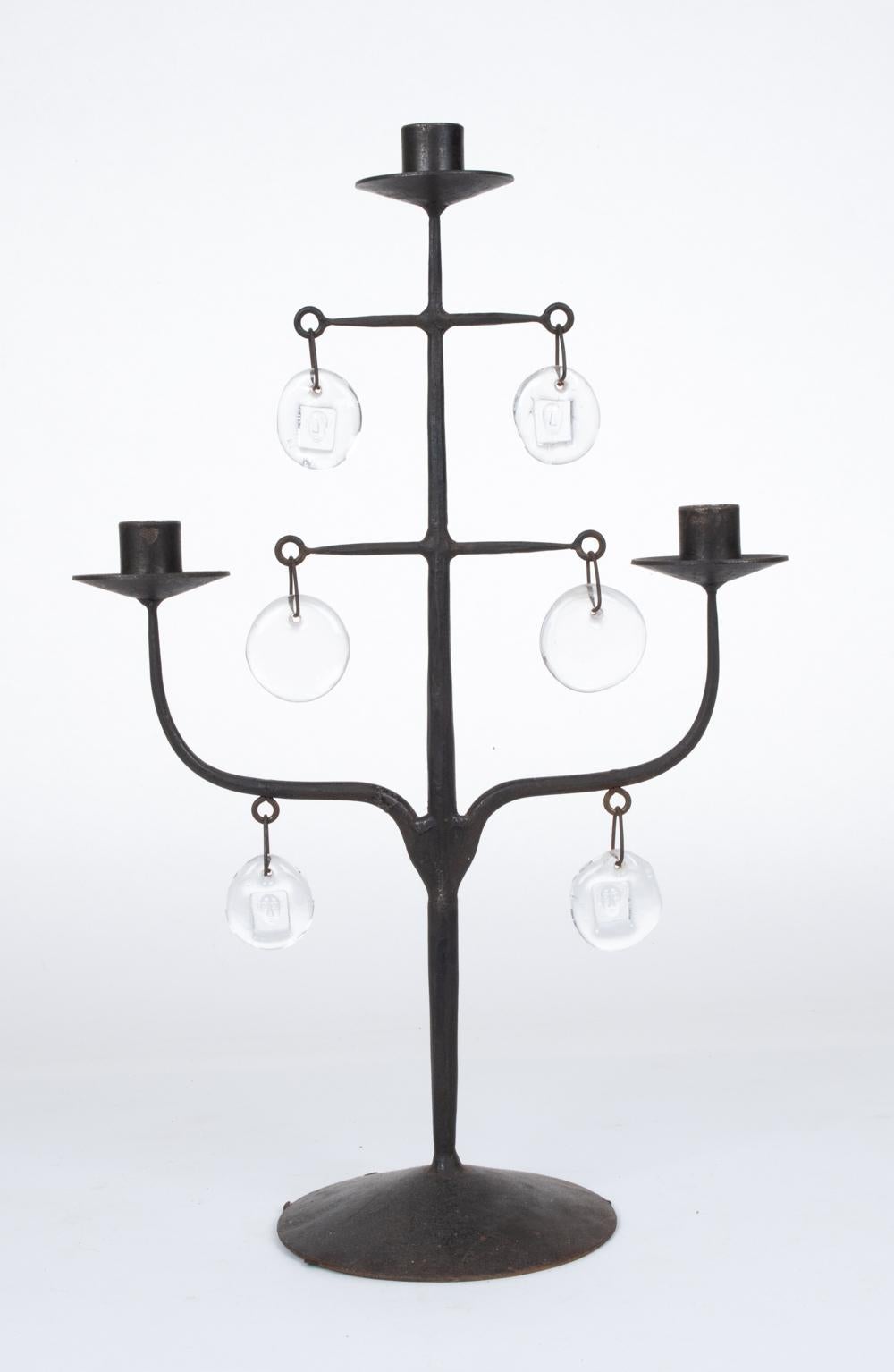A rare and unusual sculptural candelabra designed by Erik Hoglund for Boda Nova, Sweden. This three-light candle holder features a hand-crafted body of forged iron with Boda glass medallion drops, four of which are sculpted with impressed modernist