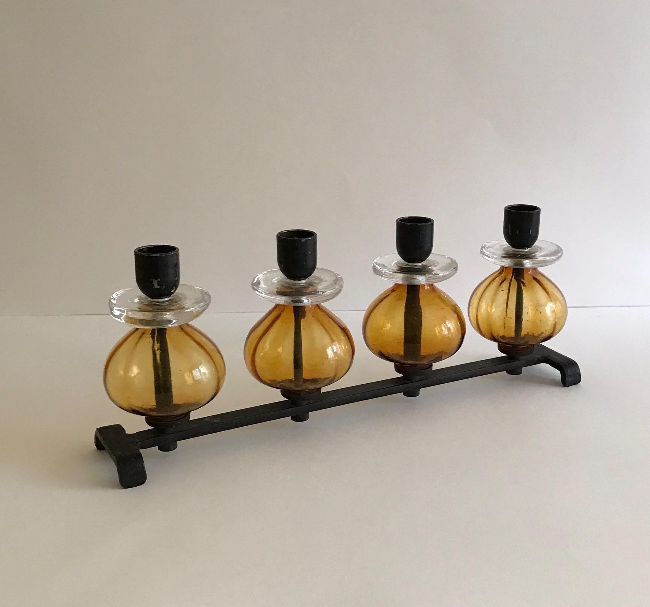 Elongated candelabra with 4 candleholders designed by Erik Hoglund for Kosta Boda glassworks, Sweden. Amber and clear glass elements on a hand forged black painted iron frame. Stamped BODA on the base

Size is 13.5” L X 5.5” H X 2.75” W.
   