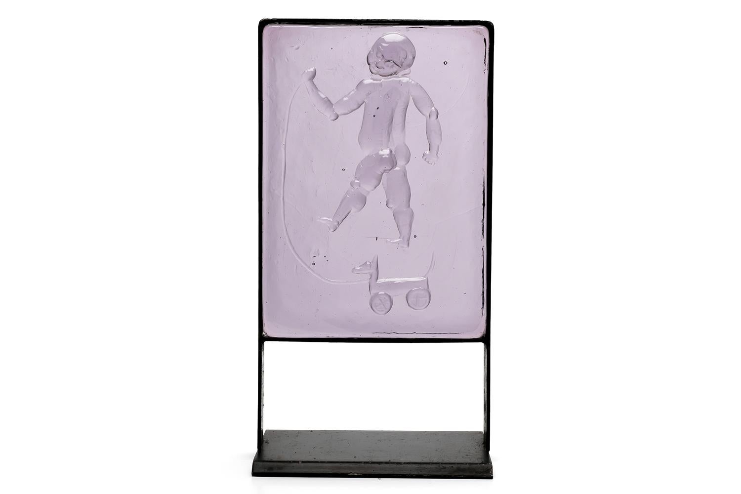 An object made of solid glass framed with black steel. The surface of the rare purple glass block is embossed with a relief of a naked baby pulling a playground equipment. 

ERIK HÖGLUND / 1932-1998 / SWEDEN
After studying sculpture at Konstfack