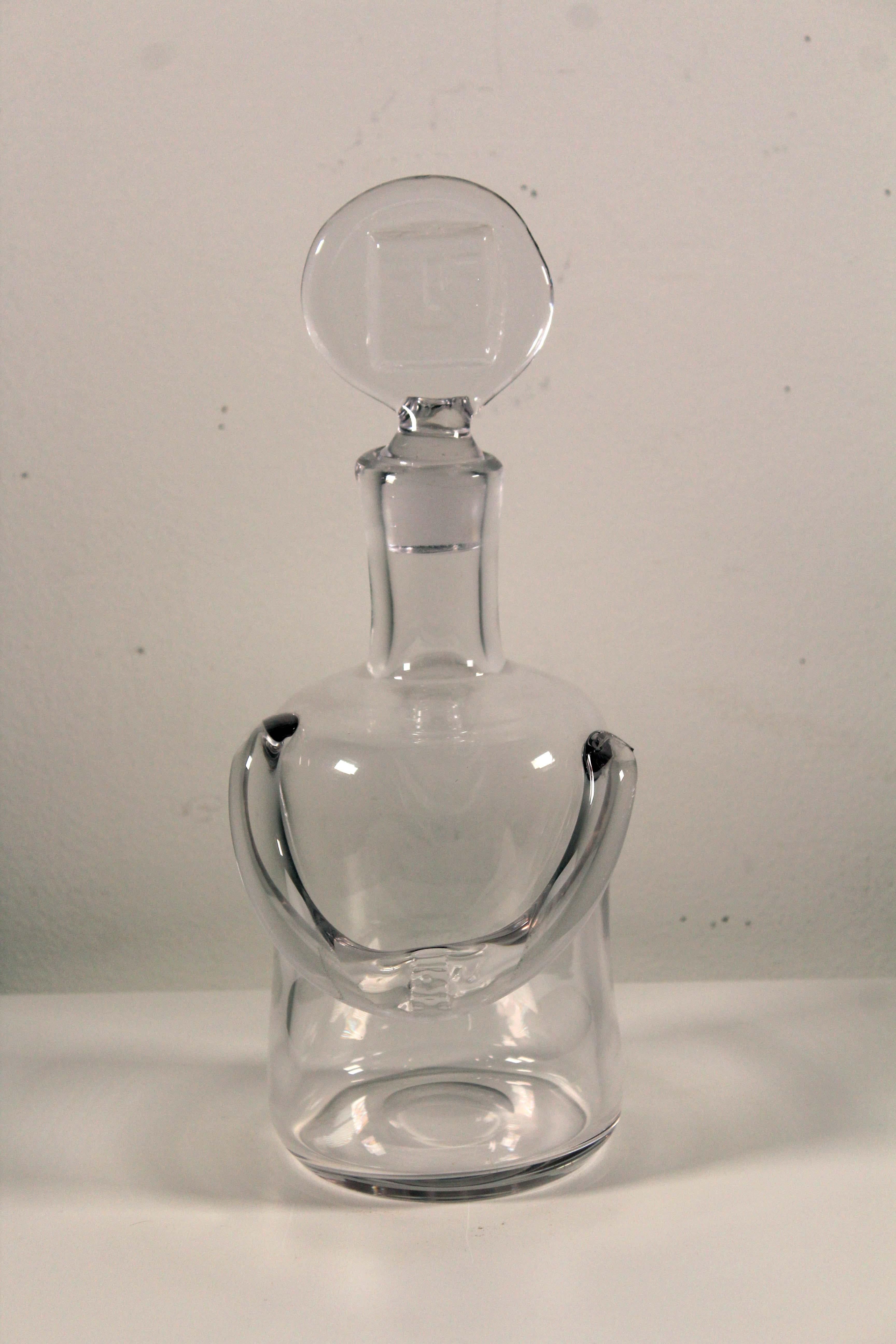 An iconic Mid-Century Modern clear glass decanter by Swedish artist Erik Hoglund. The lid of the bottle has his infamous male face design. Etched on bottom H. / 346 / 65. From a private collection. Dimensions: 11.5” height x 4.5” diameter. In very