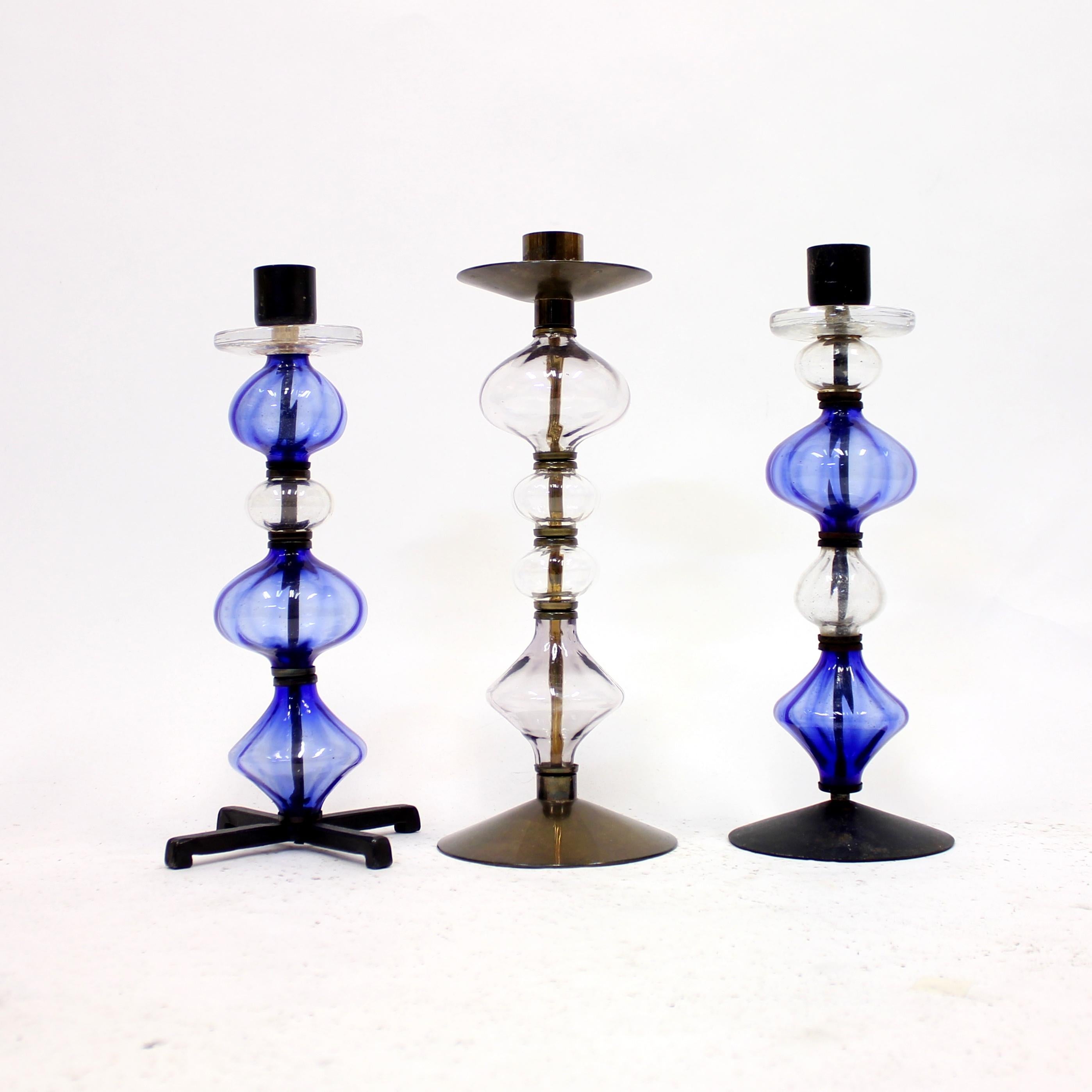 Set of three large candle holders by Erik Höglund in glass and wrought iron and brass. Made by Swedish manufacturer Boda Glasbruk & Smide in the 1960s. Base and frame made of wrought iron with blue and clear glass decoration. Diameter of the bases