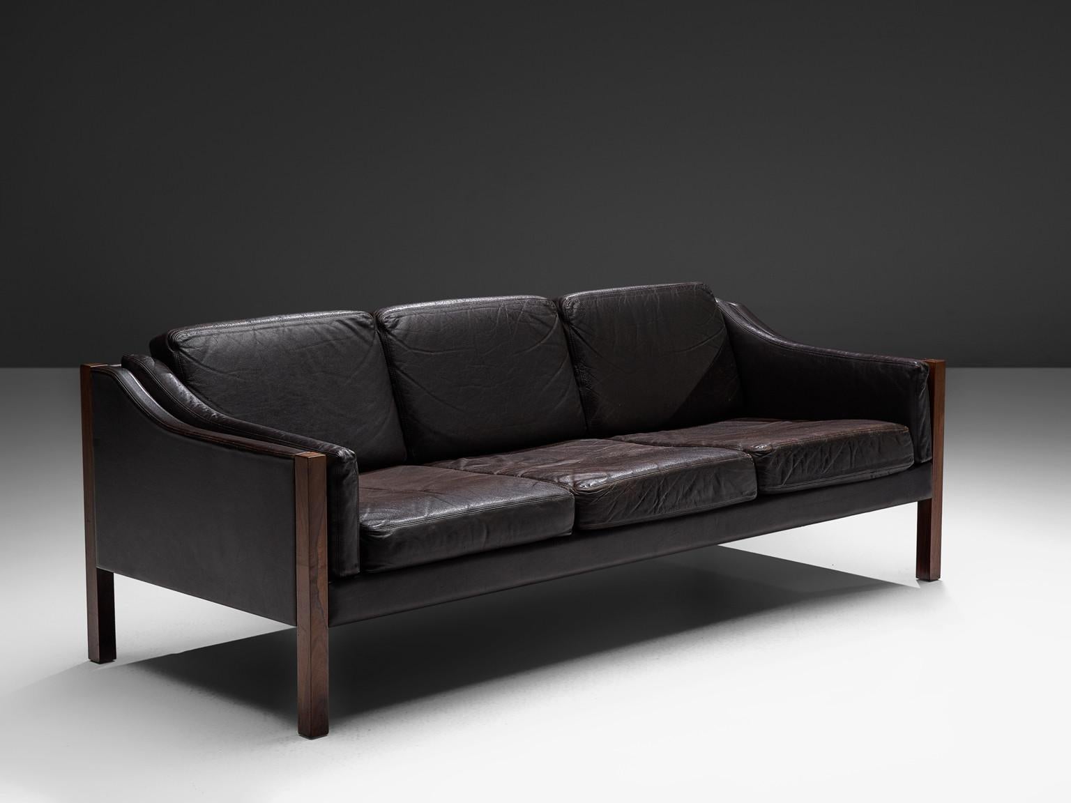 Erik Jørgensen, settee, in dark brown leather and rosewood, Denmark, 1963.

This sofa by Jørgensen features an elegant design. This sofa has a low, curved back, which smoothly runs over into the armrests with detailed piping. Seating and back