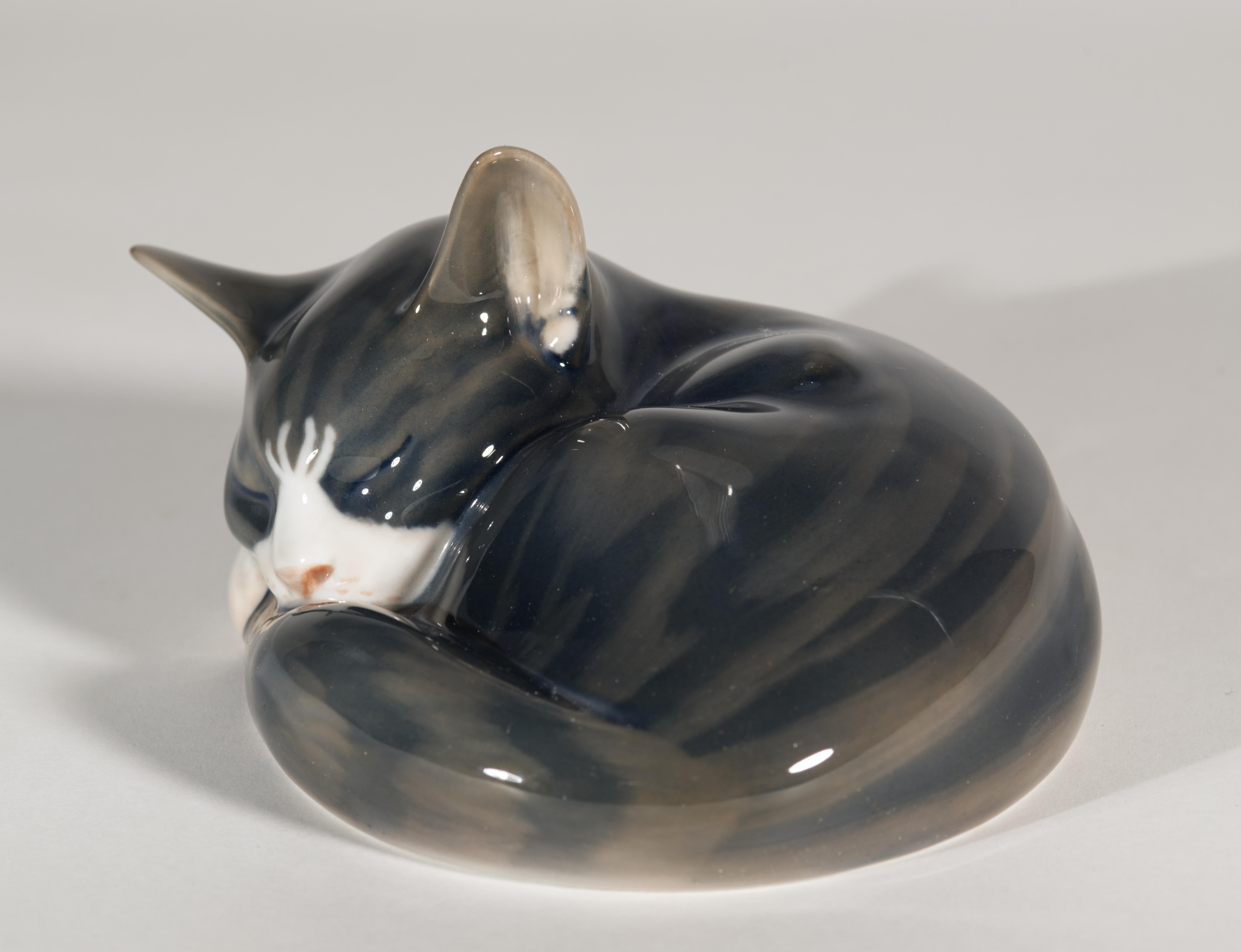 L'affascinante scultura vintage di un gatto soriano grigio e bianco che dorme è stata disegnata da Erik Nielsen per Royal Copenhagen. La statuetta di porcellana altamente dettagliata è stata decorata a mano con particolare attenzione al muso, alle
