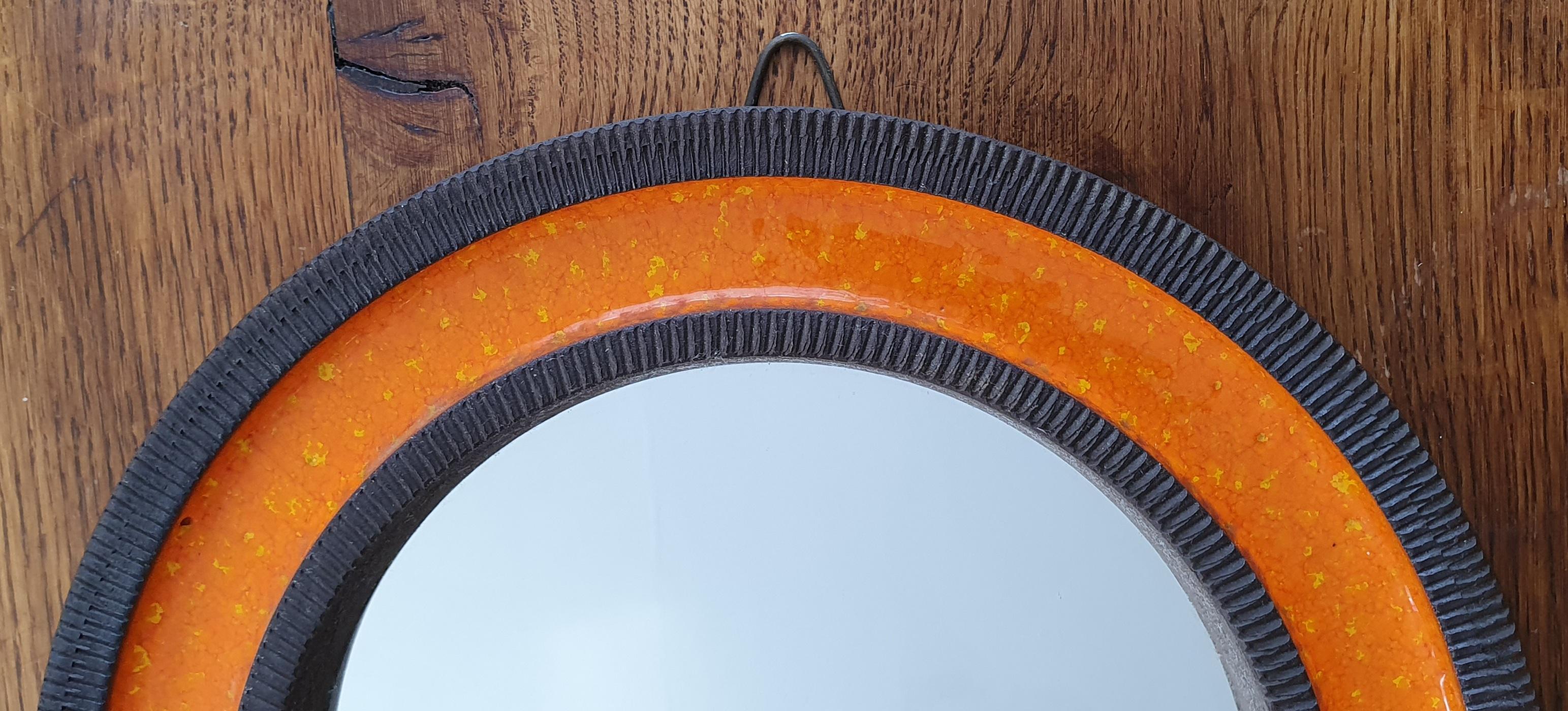 Orange midcentury round ceramic wall mirror designed by Erik Reiff for Danish Knabstrup. The mirror is made of glazed ceramic and has alternating rings with a ceramic ribbed edge and a smooth orange crystalline glaze on the inside. This color is