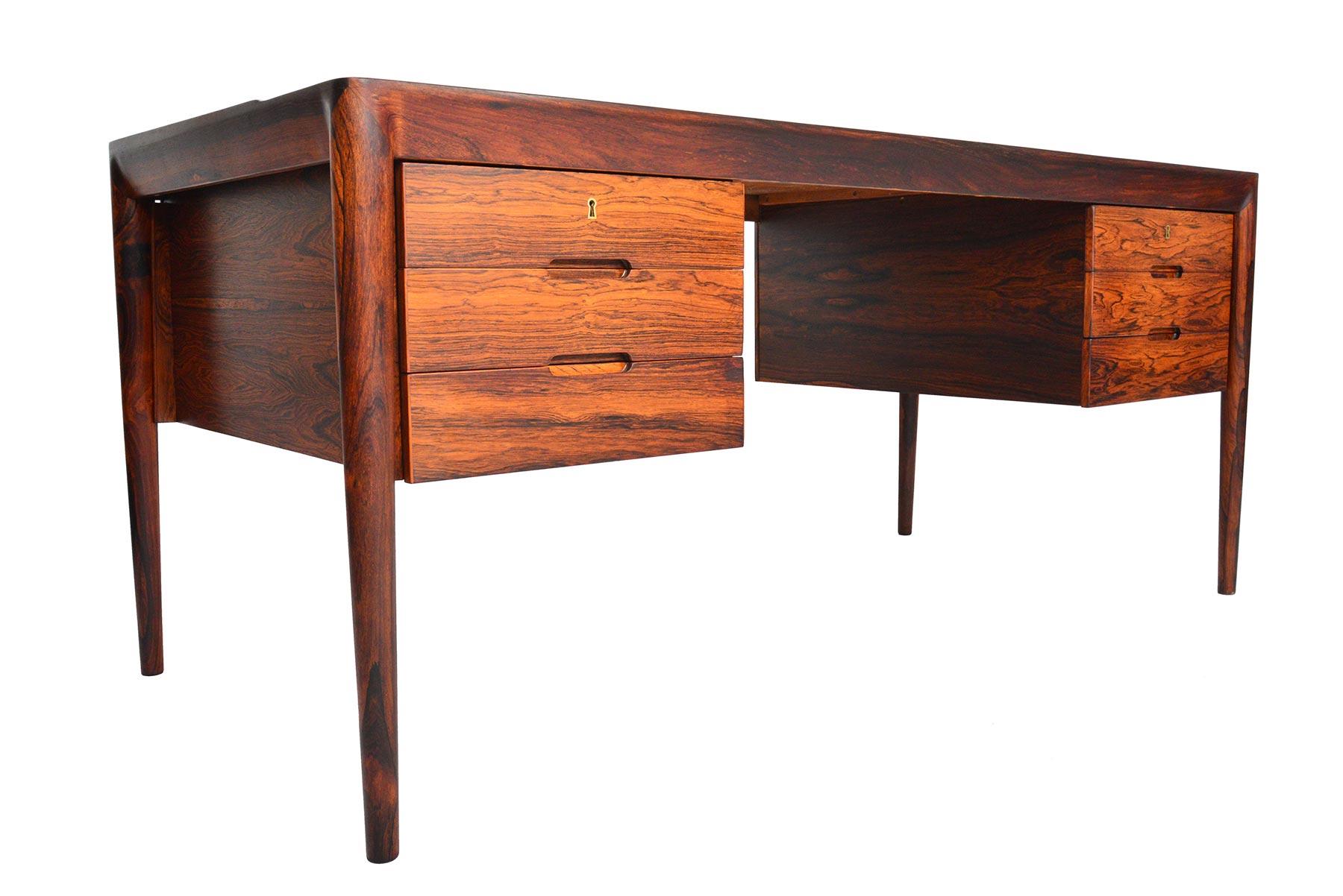 This rare Danish modern executive desk was designed by Erik Riisager Hansen for Haslev Møbelsnedkeri in the 1960s. The beautiful banding seamlessly joins to the exterior mounted legs. Crafted in Brazilian rosewood, the top slab features a raised lip