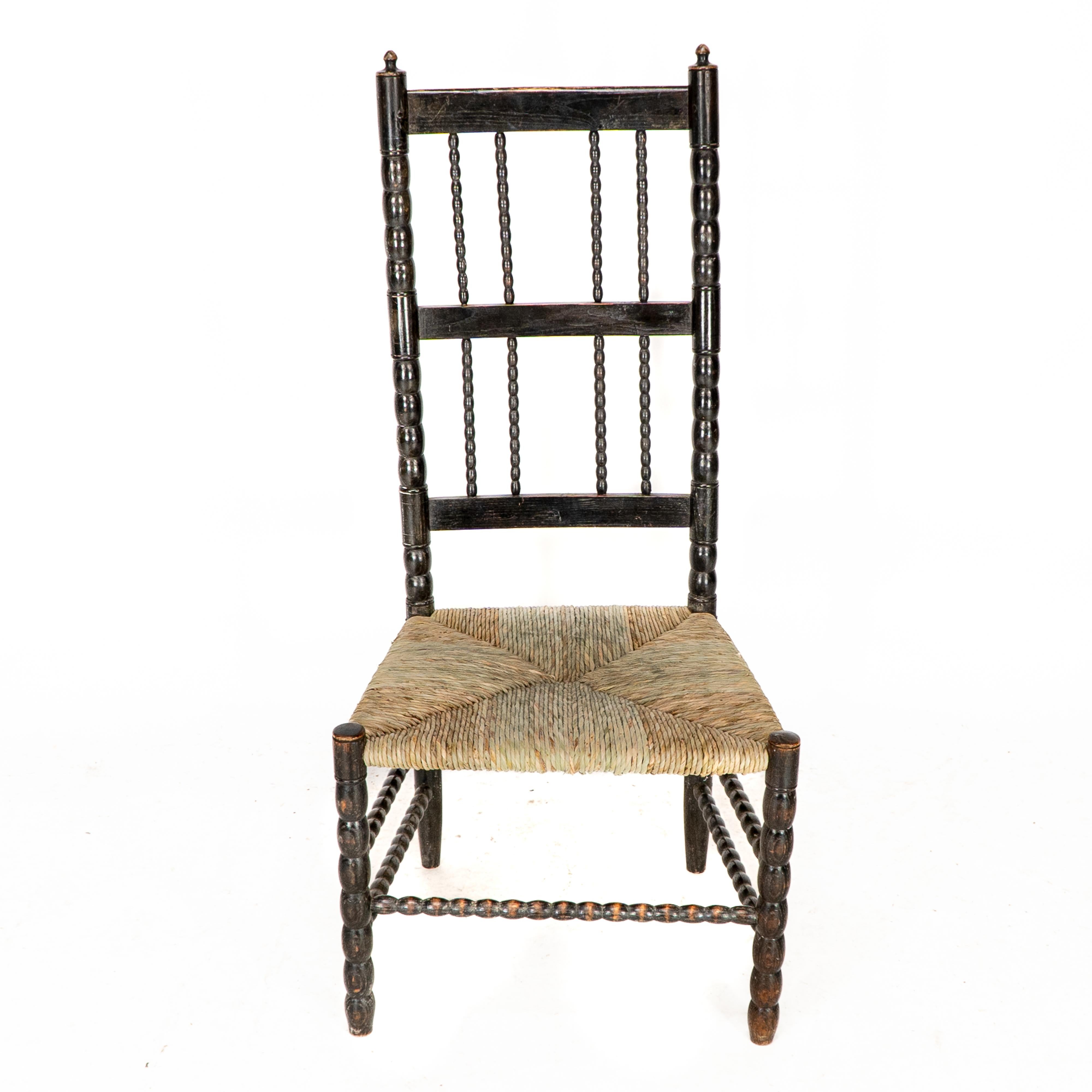 Ernest Gimson. Rare chaise basse de l'école de Cotswold, ébonisée, tournée aux fuseaux et à l'assise en jonc, avec des épis de faîtage tournés et des chevilles à chaque joint et une assise en jonc nouvellement posée. L'assise de ce fauteuil a été