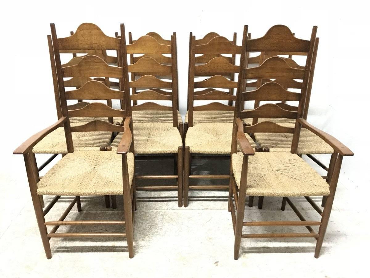 After a design by Ernest Gimson. A set of ten high back Arts & Crafts Cotswold School oak ladder back dining chairs consisting of two armchairs and eight side chairs with through tenon details to the shaped arms at the fronts and rope twist sea