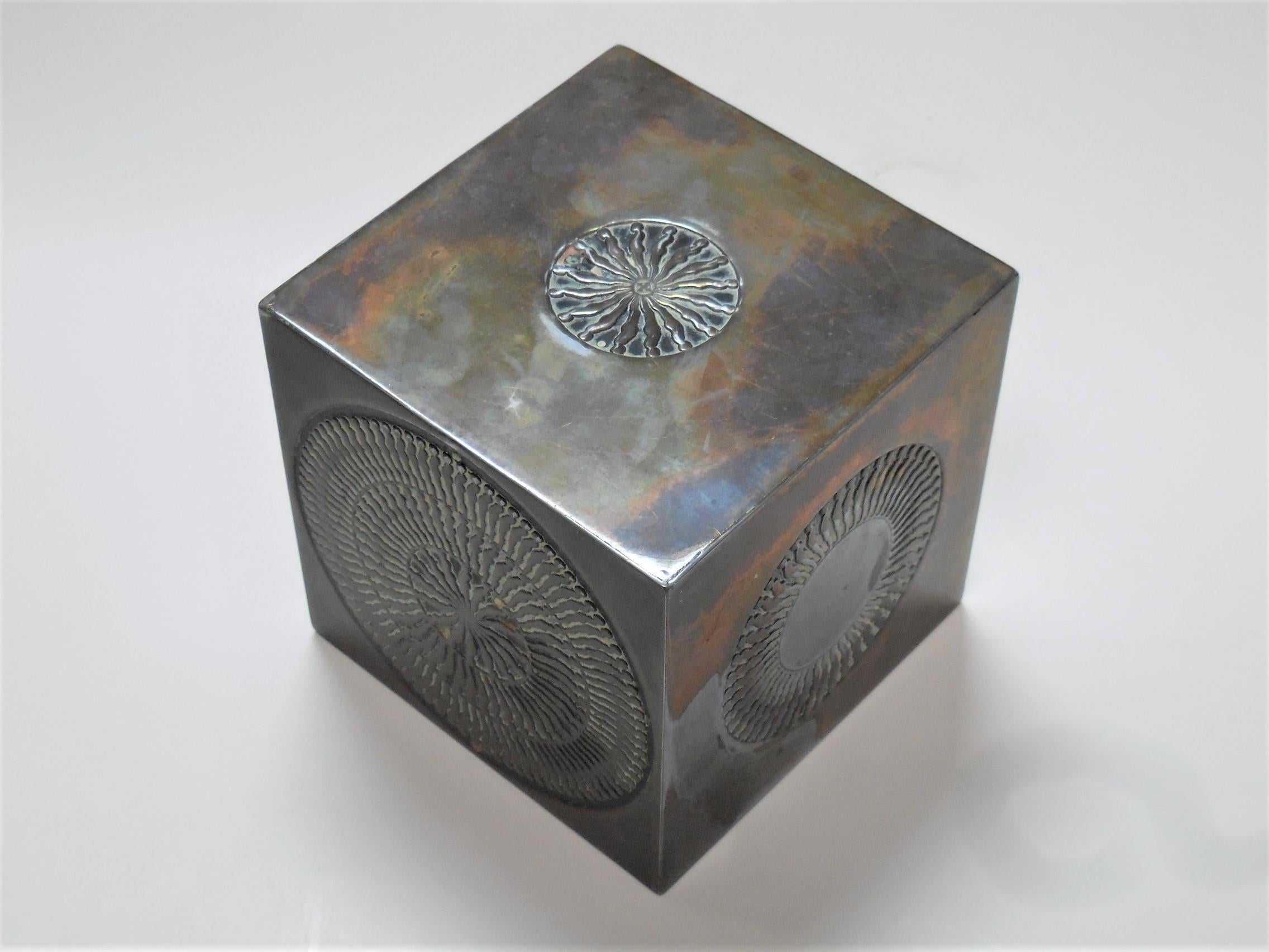A cube sculpure by Trova. It is bronze with a worn nickel plated finish. All surfaces include representations of his iconic falling man within a circle.