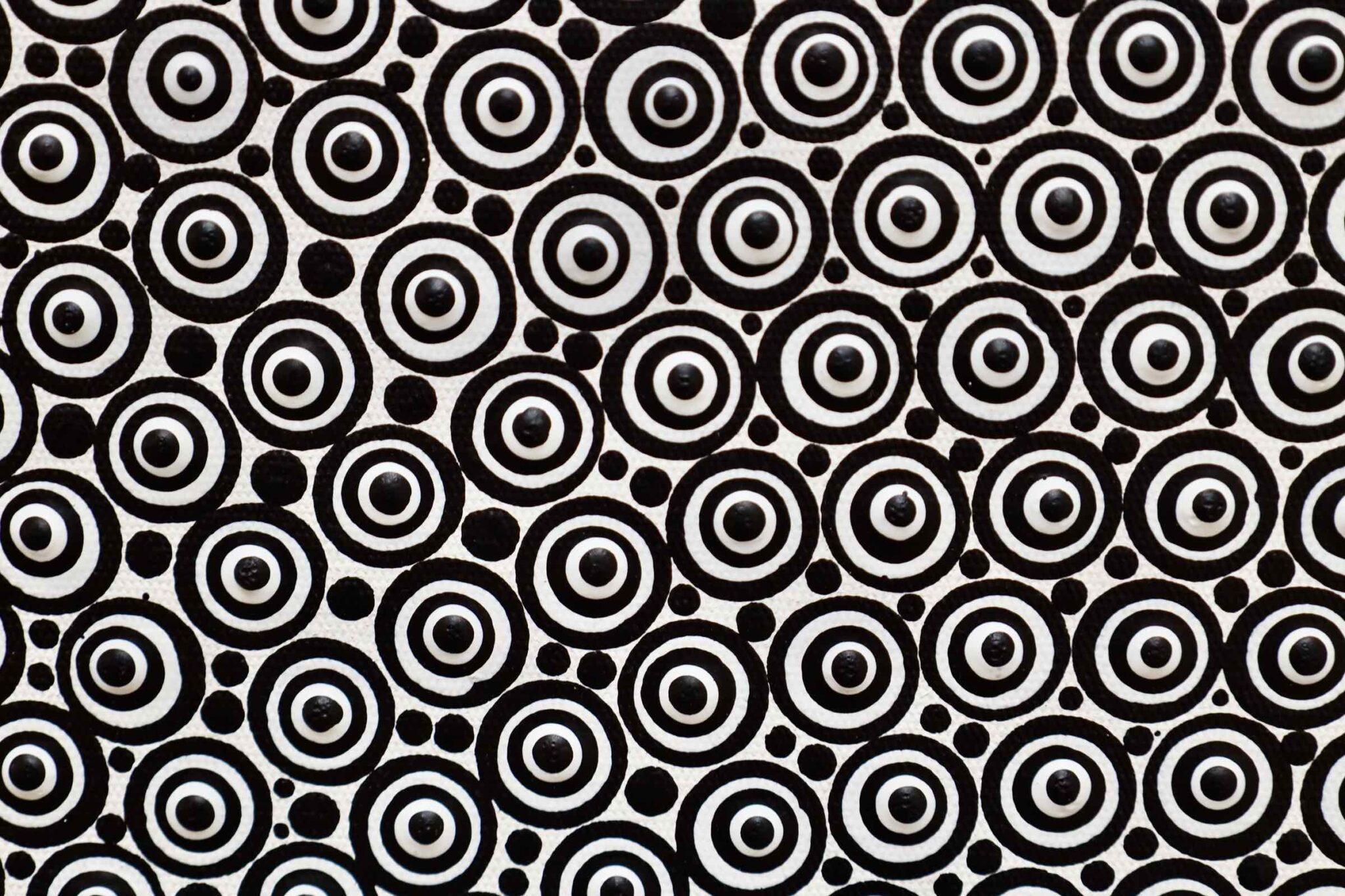 In the work “Synergy” by Ernesto Guevara the artist features an intriguing geometric composition centered on a large circle filled with multiple small, concentric rings, each made up of even smaller detailed patterns that create a sense of depth and